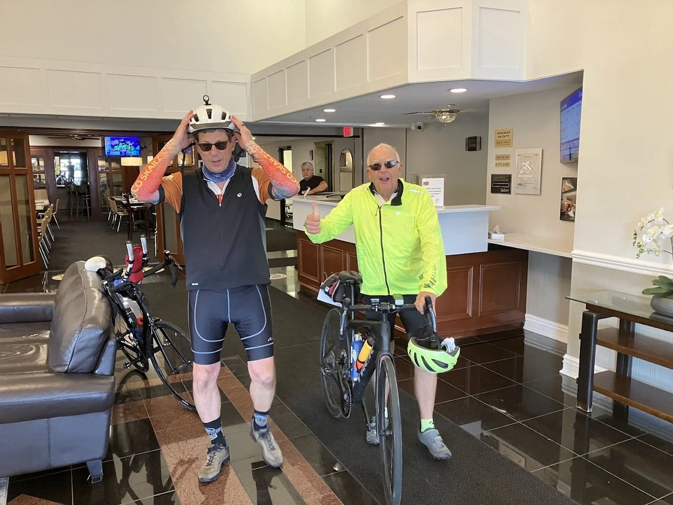 Image of two men in a hotel lobby, both with their bikes.  The gentlemen on the right is giving a thumbs up.