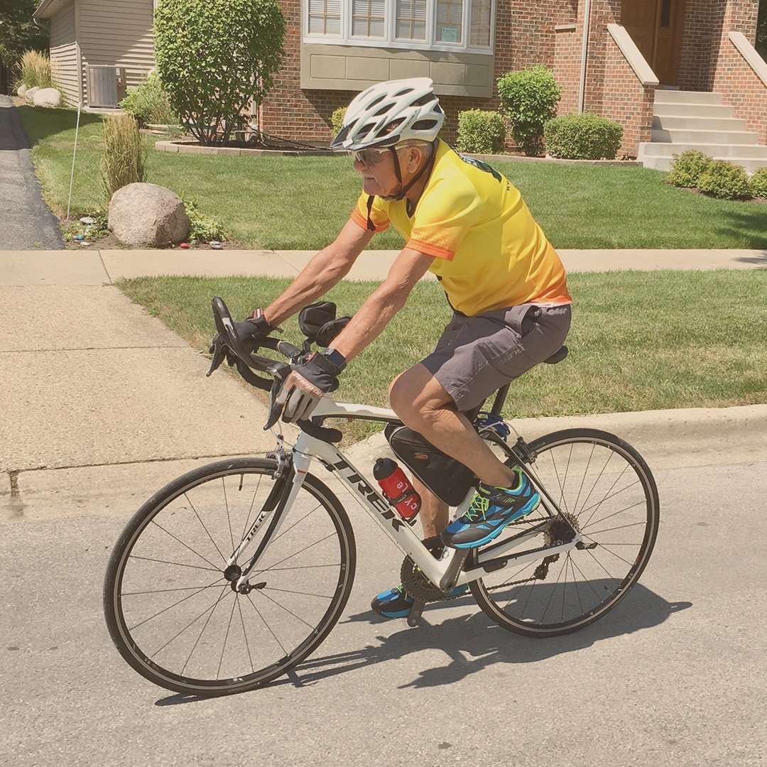 Gentlemen seen riding a white bike while in a bright yellow cycling jersey and wearing a white helmet.