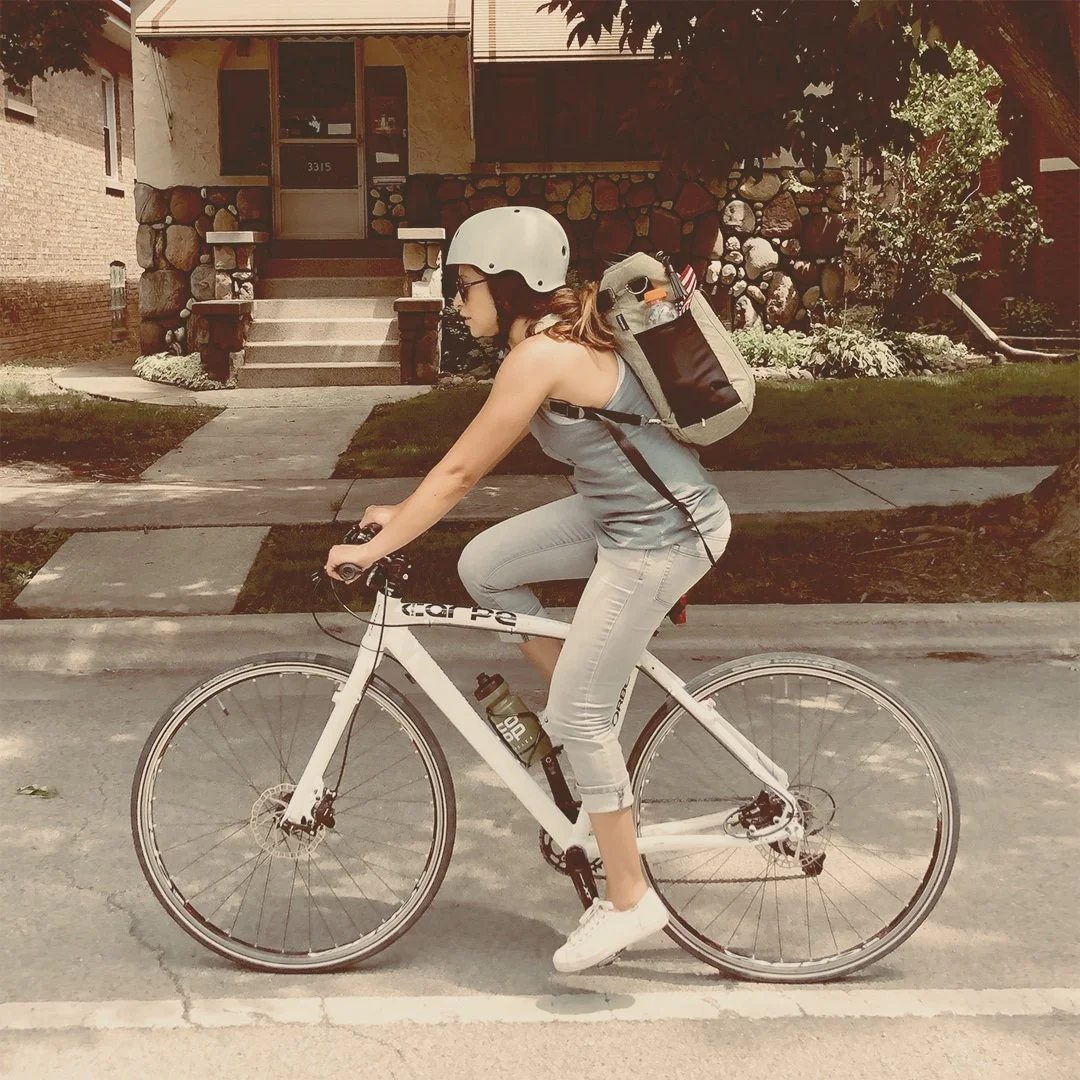 Female bicyclist pictured riding a white bike while wearing a helmet and carrying a backpack.