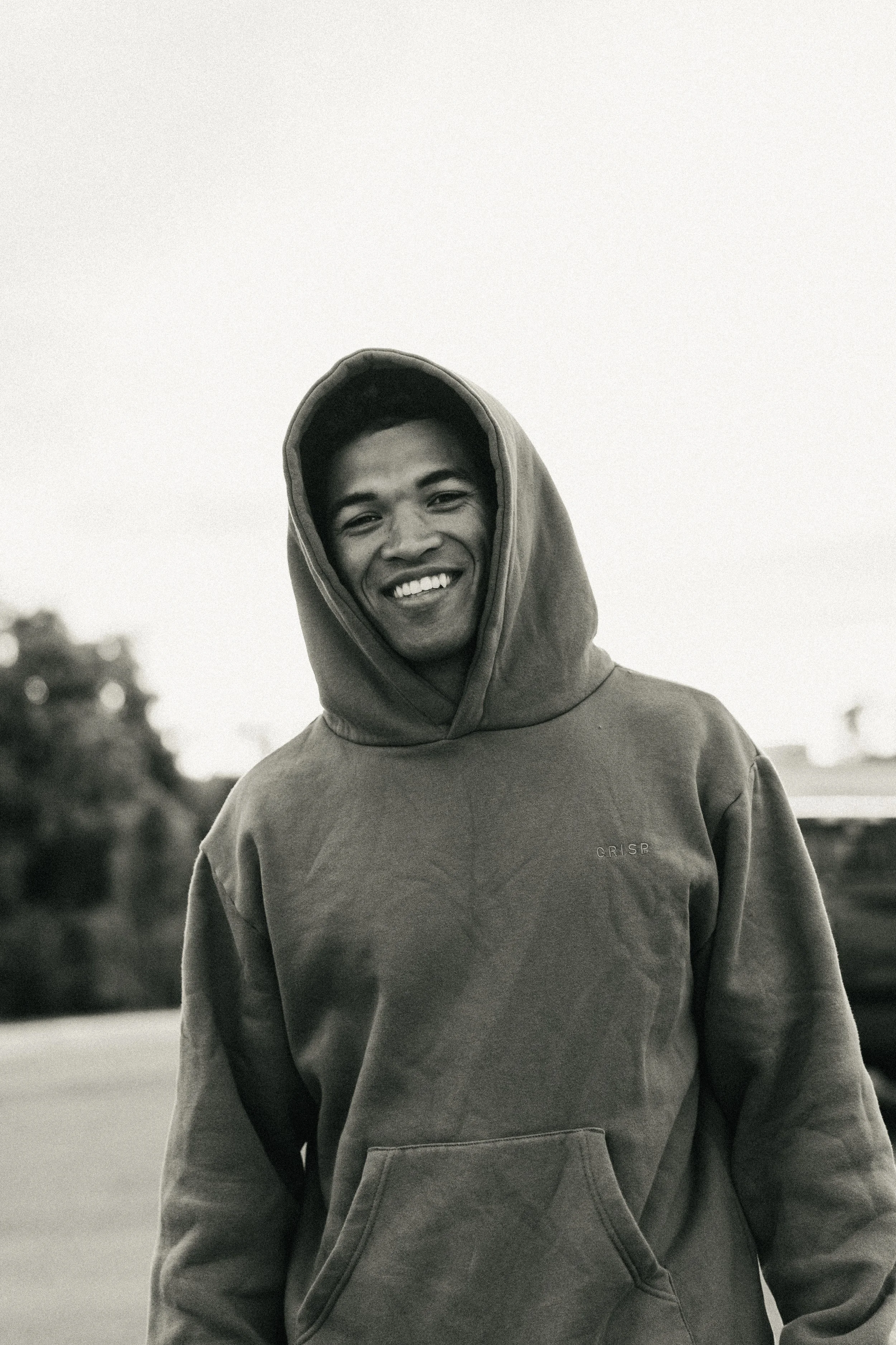 A young man smiling outdoors wearing a hoodie in black and white.