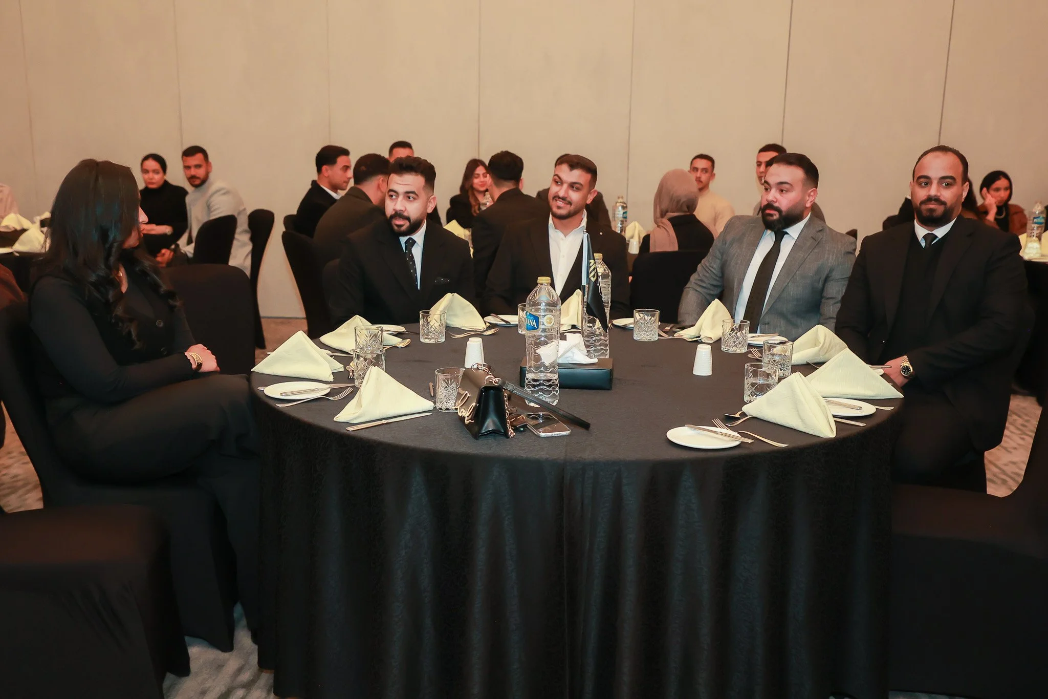 Group of people in formal attire sitting around a round banquet table at a formal event or conference.