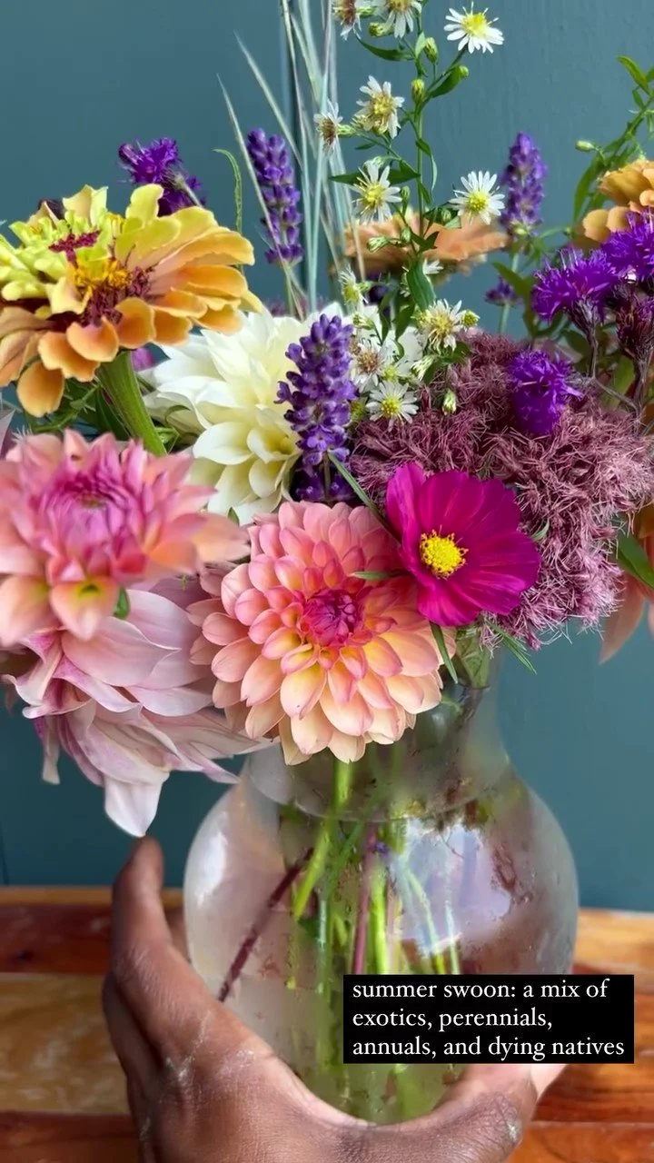 A colorful bouquet of summer flowers including dahlias, cosmos, lavender, and daisies in a glass vase.