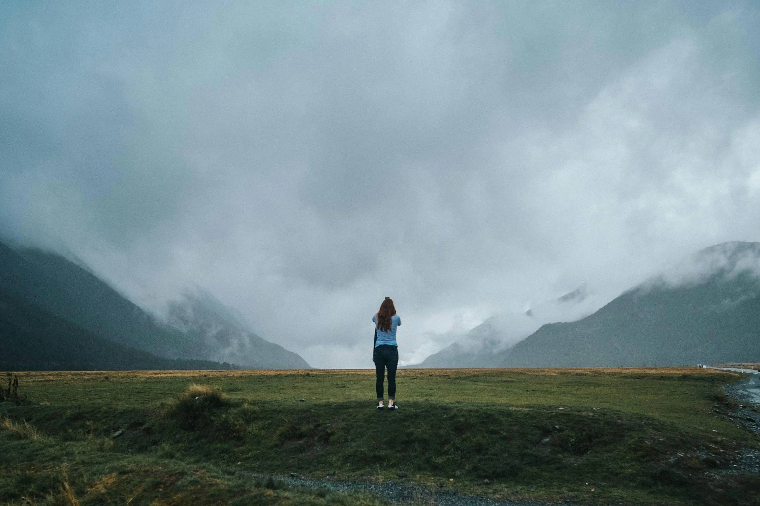 A woman stands facing fog-covered mountains, representing feeling stuck, uncertainty, and seeking clarity through therapy.