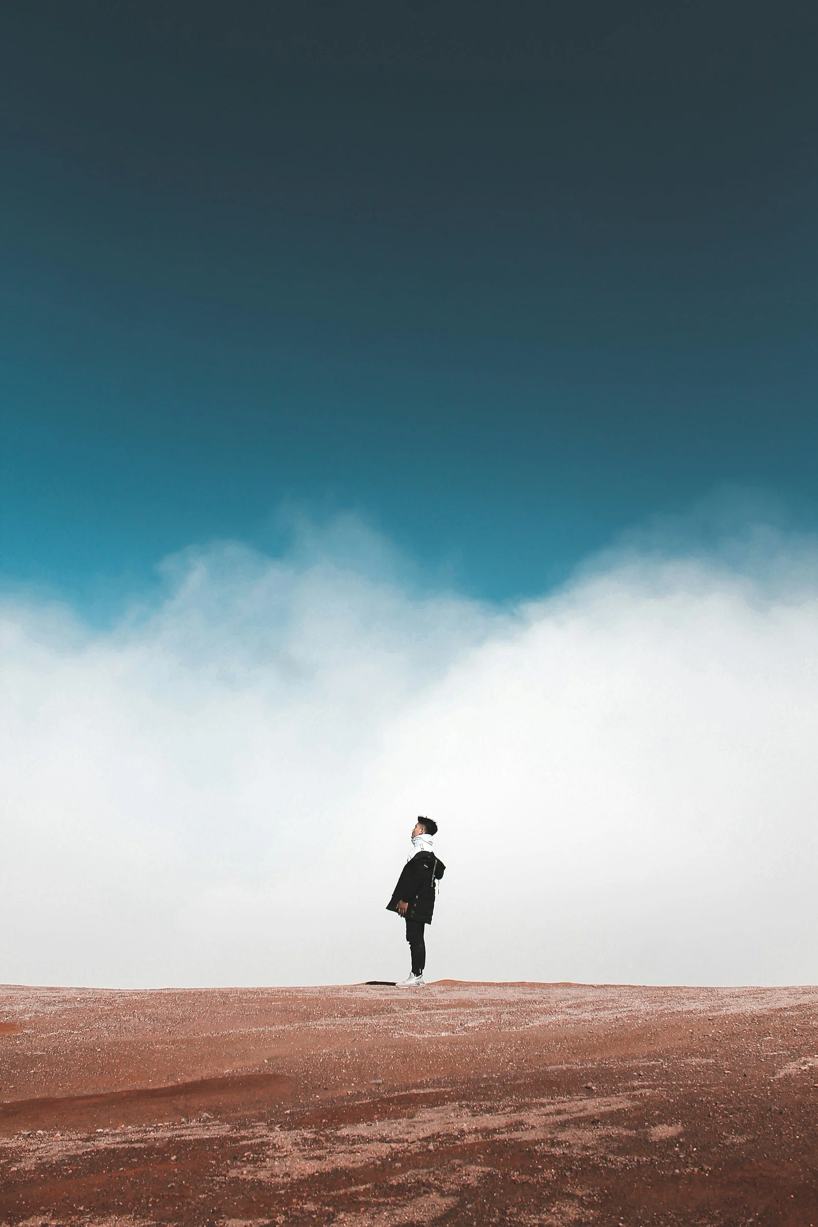 A person standing beneath expansive clouds and sky, symbolizing perspective, space, refocus, and emotional clarity.
