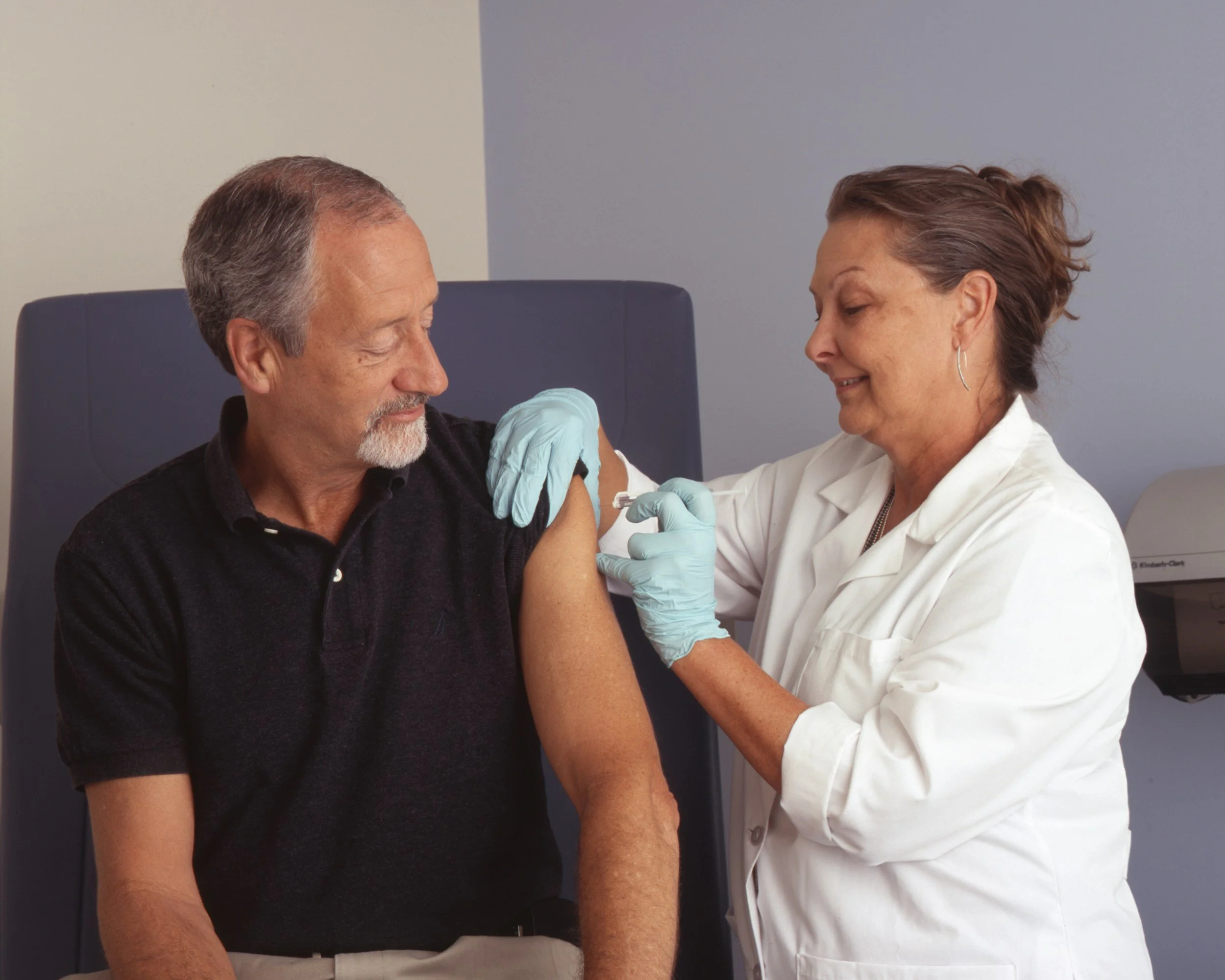 A healthcare professional administering a vaccination to a seated middle-aged man in a medical office.