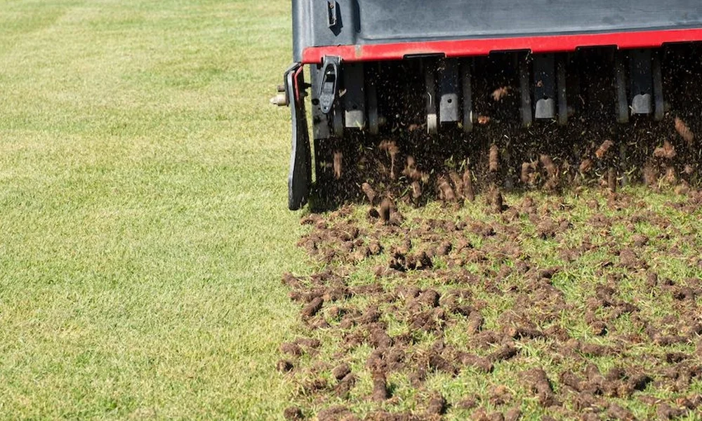 A close-up of a turf cultivator tilling the soil on a football field.