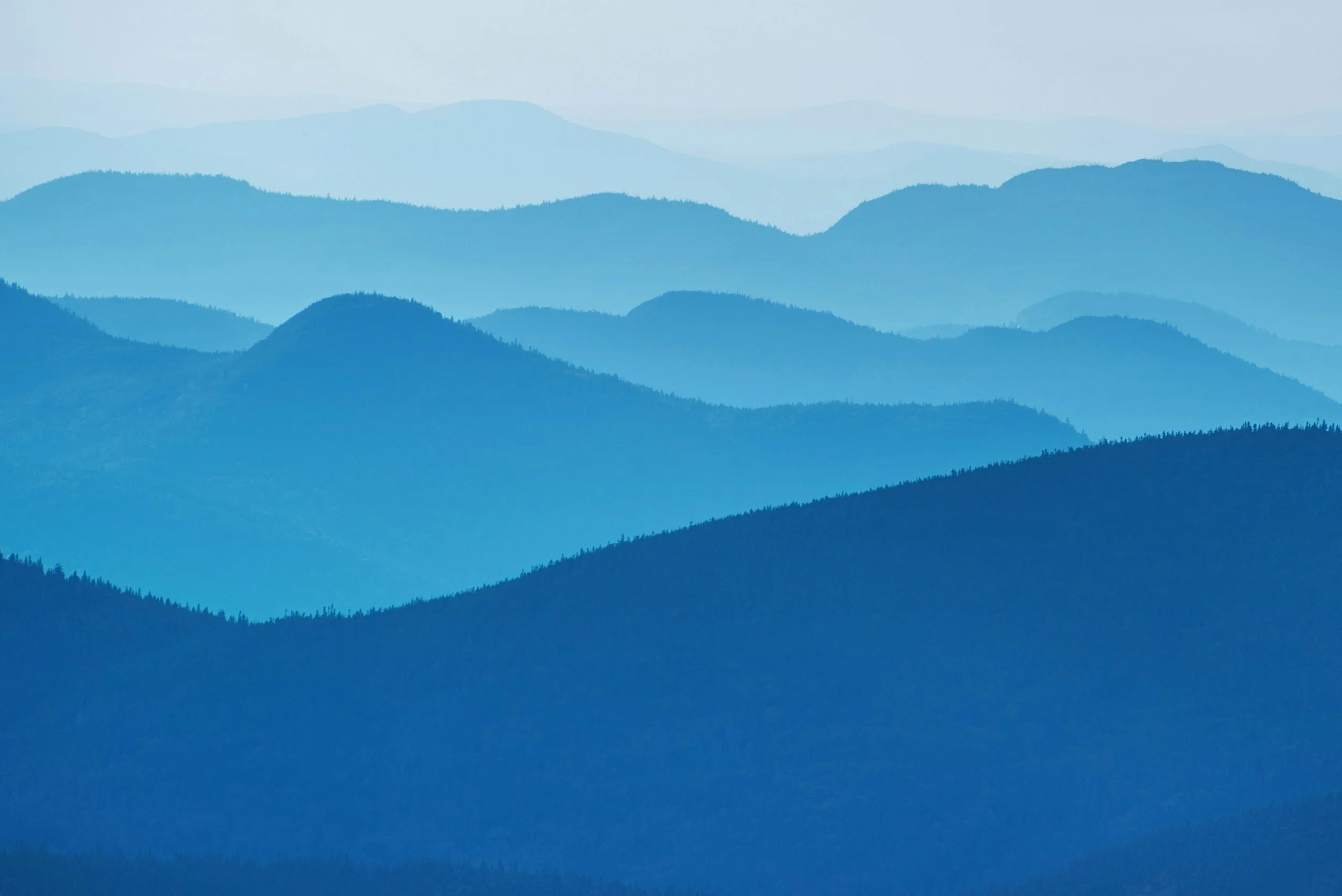 Series of blue mountain ridges overlapping in the distance with a misty atmosphere.
