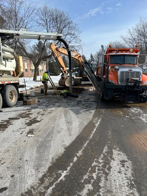 Workers repairing a water main in the street with heavy machinery during winter.