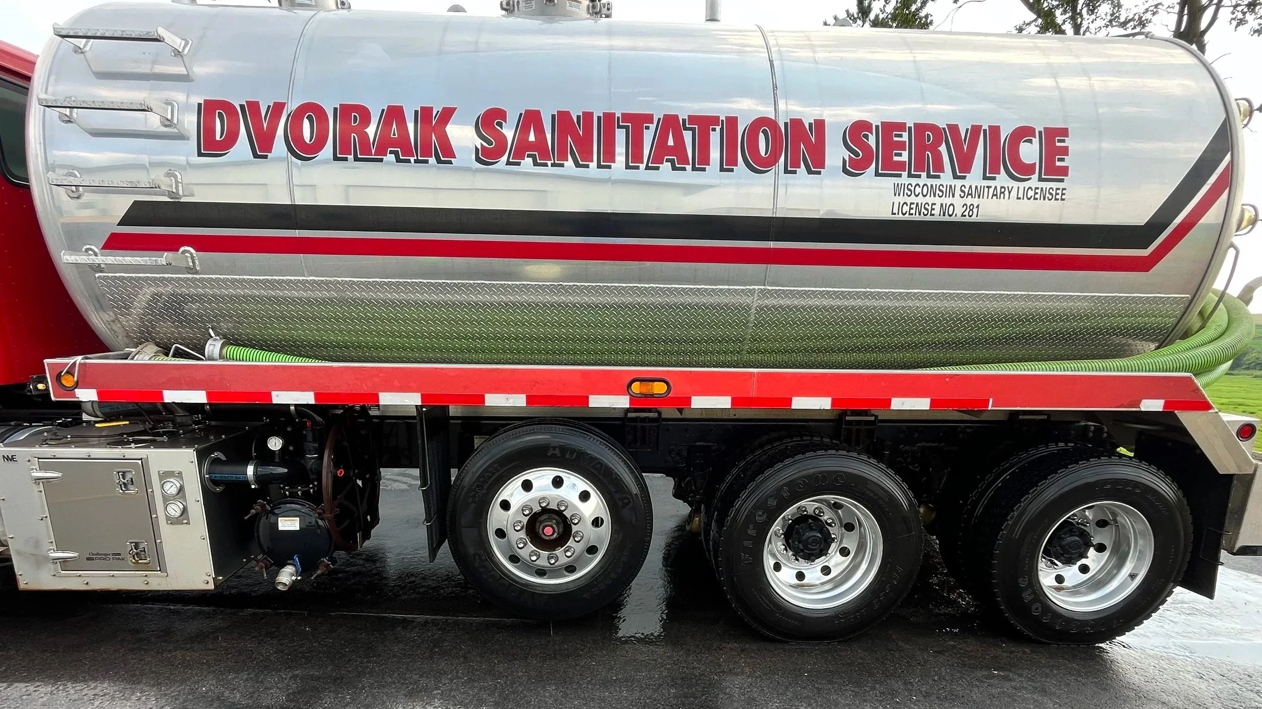 A commercial sanitation truck with the words "Dvorak Sanitation Service" written on the side, equipped with hoses and mechanical parts for cleaning or waste management.