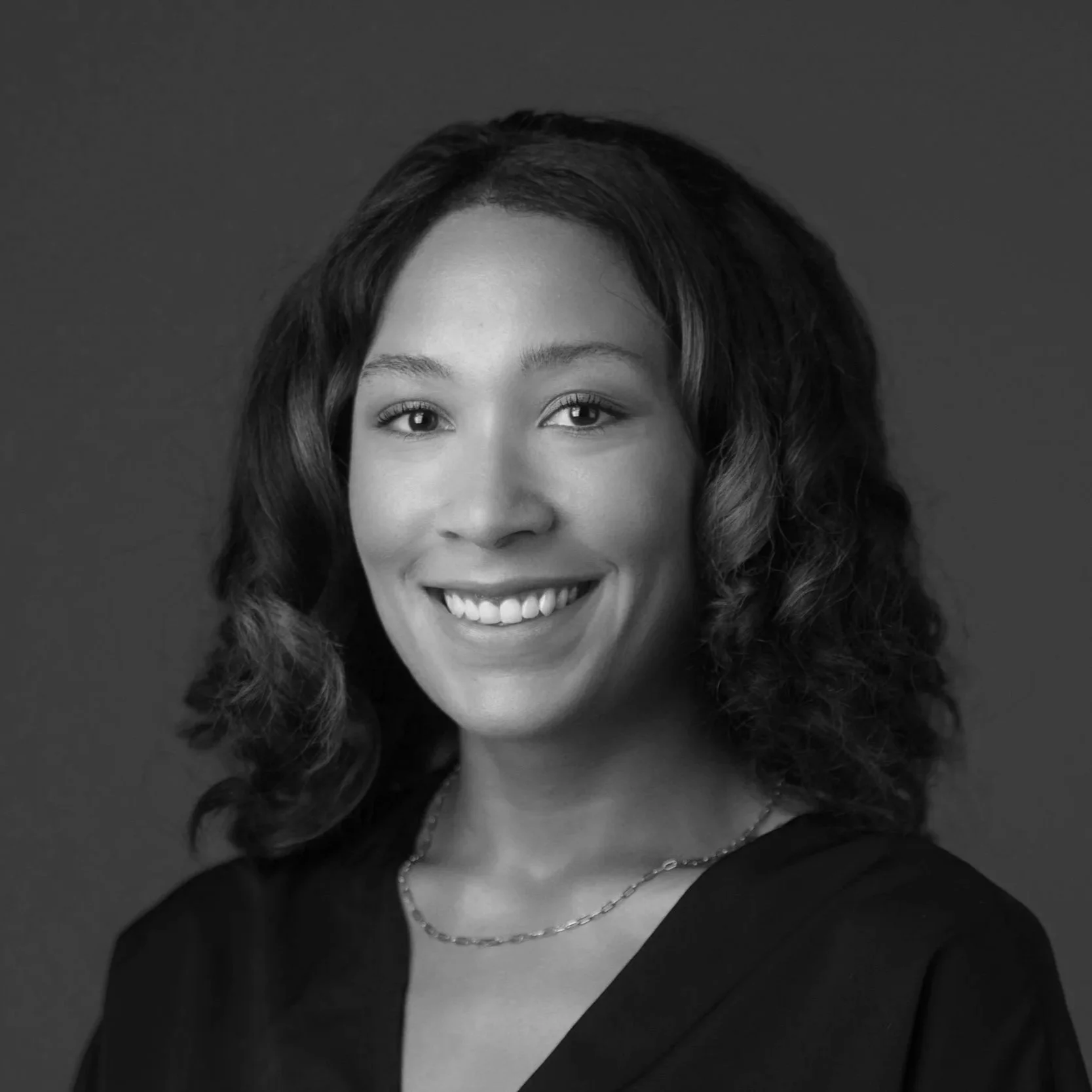 Black and white portrait of a young woman smiling, wearing a dark top and a necklace.