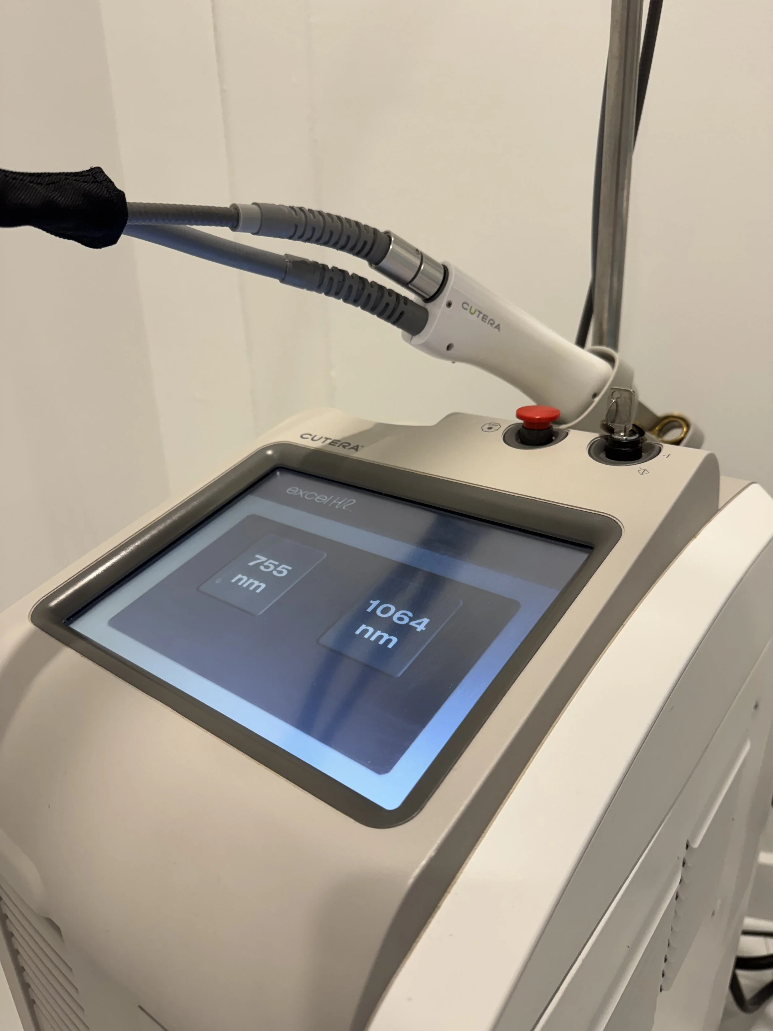 A medical examination room with a white chair and equipment, including a skull replica, and a poster of a person's abdomen in the background.