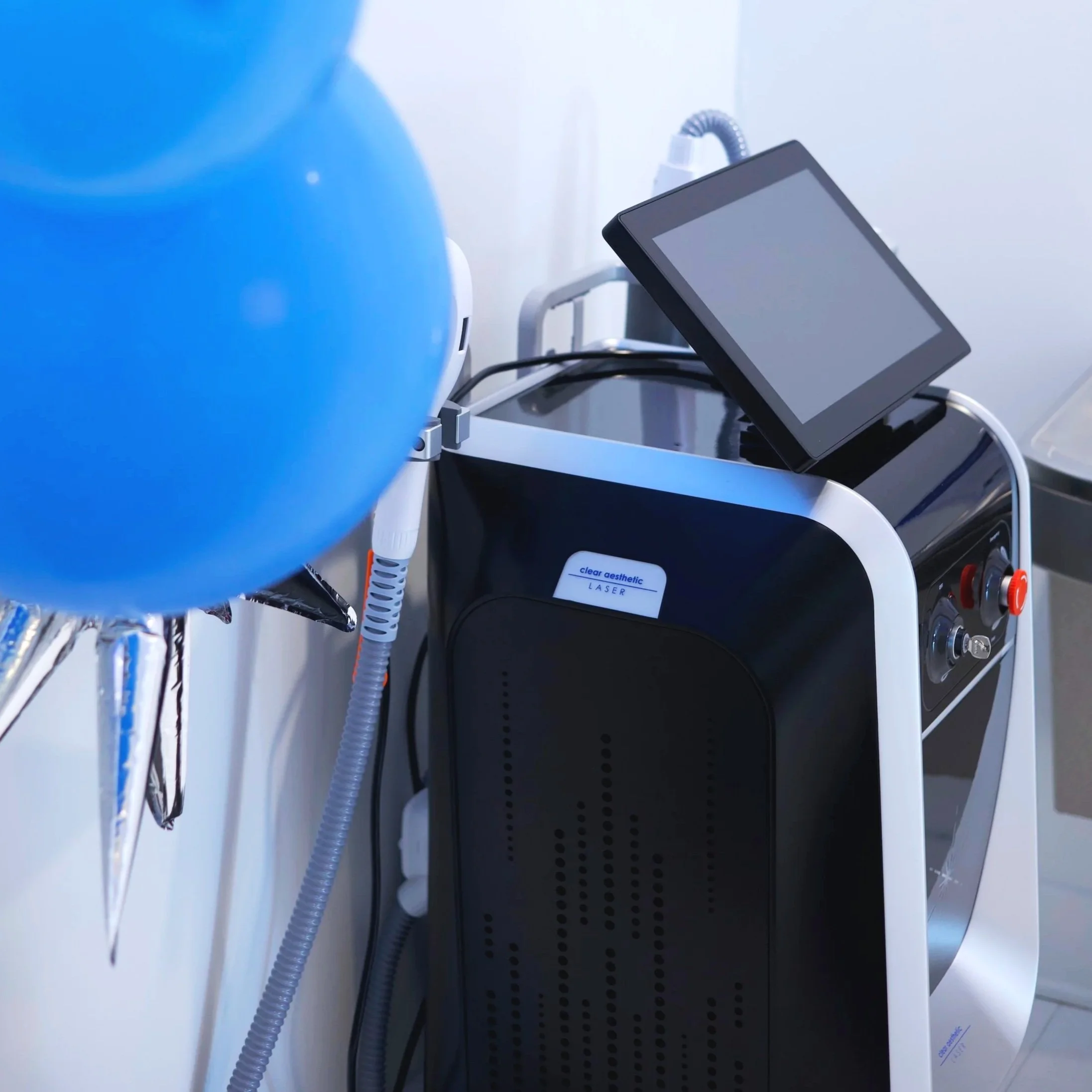 A medical examination room with a white chair and equipment, including a skull replica, and a poster of a person's abdomen in the background.