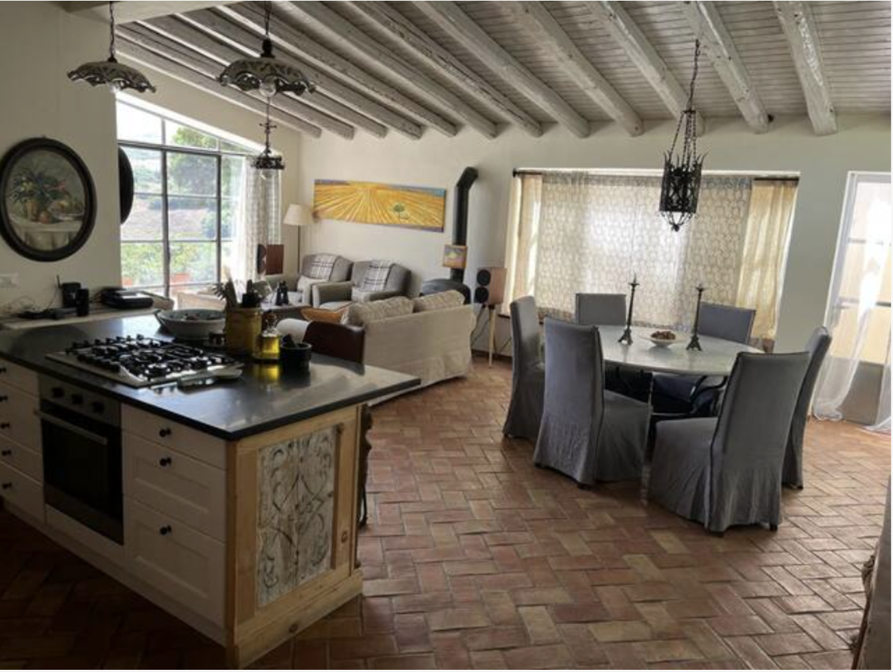 Open-concept living room and dining area with a kitchen island, sofa, armchairs, dining table with six chairs, and large windows allowing natural light.