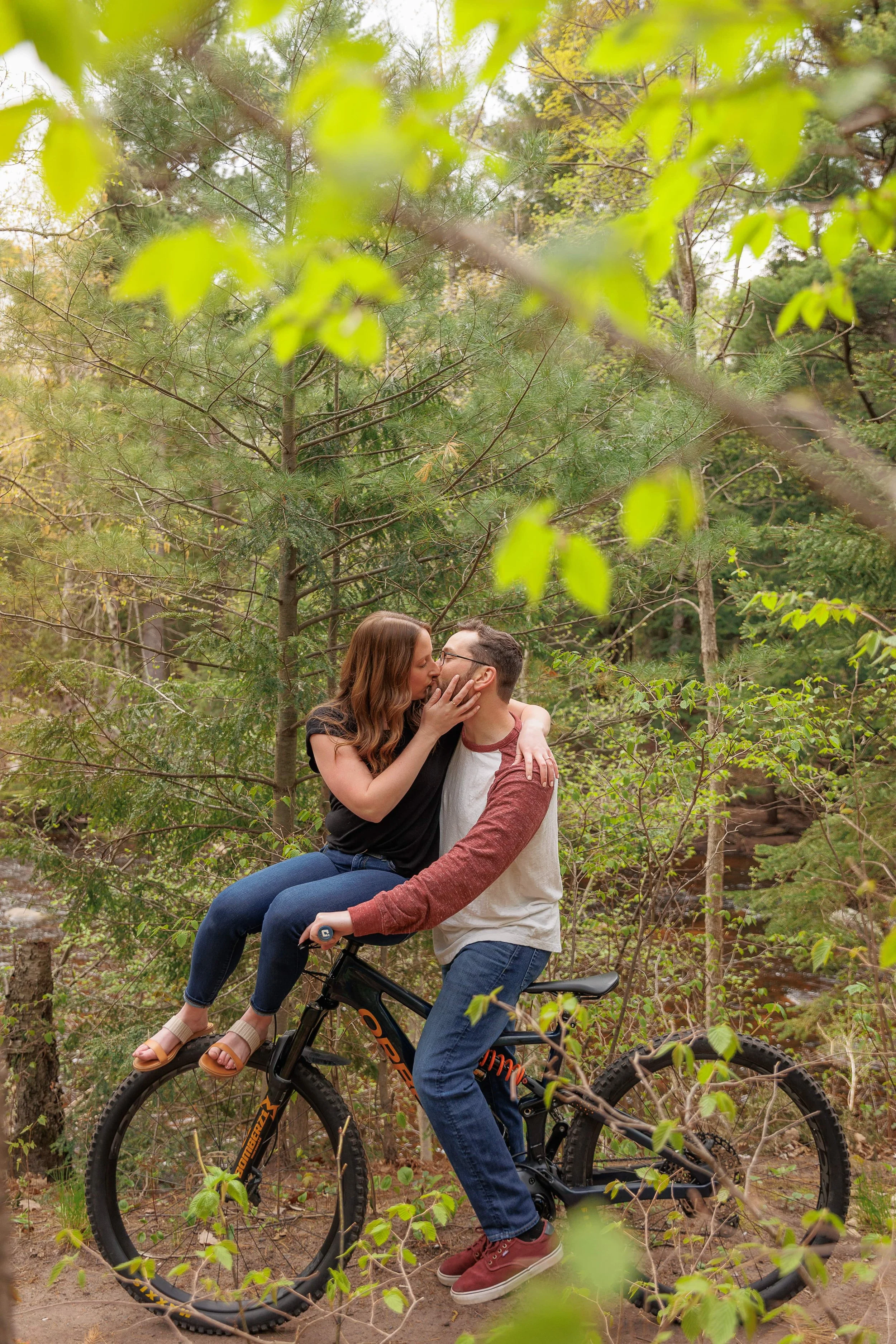 Couple kissing on a bicycle in a forest setting