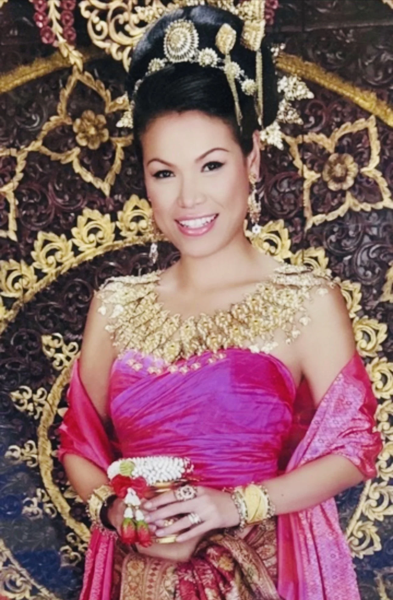 A Southeast Asian woman in a  black dress holding a wine glass, smiling, against a garden back drop