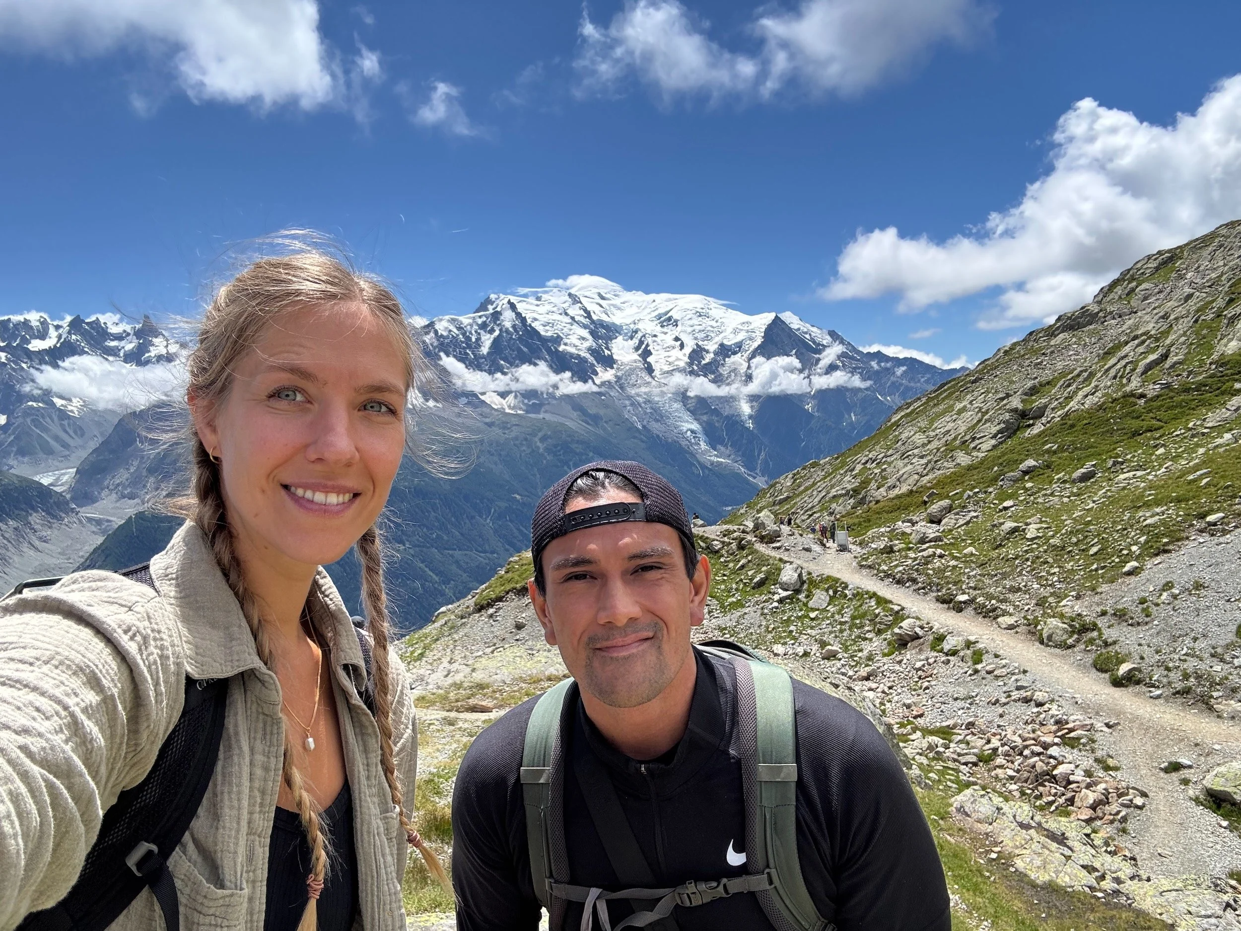 Nora and Trevor hiking on a mountain trail with the Mont Blanc massif in the background.