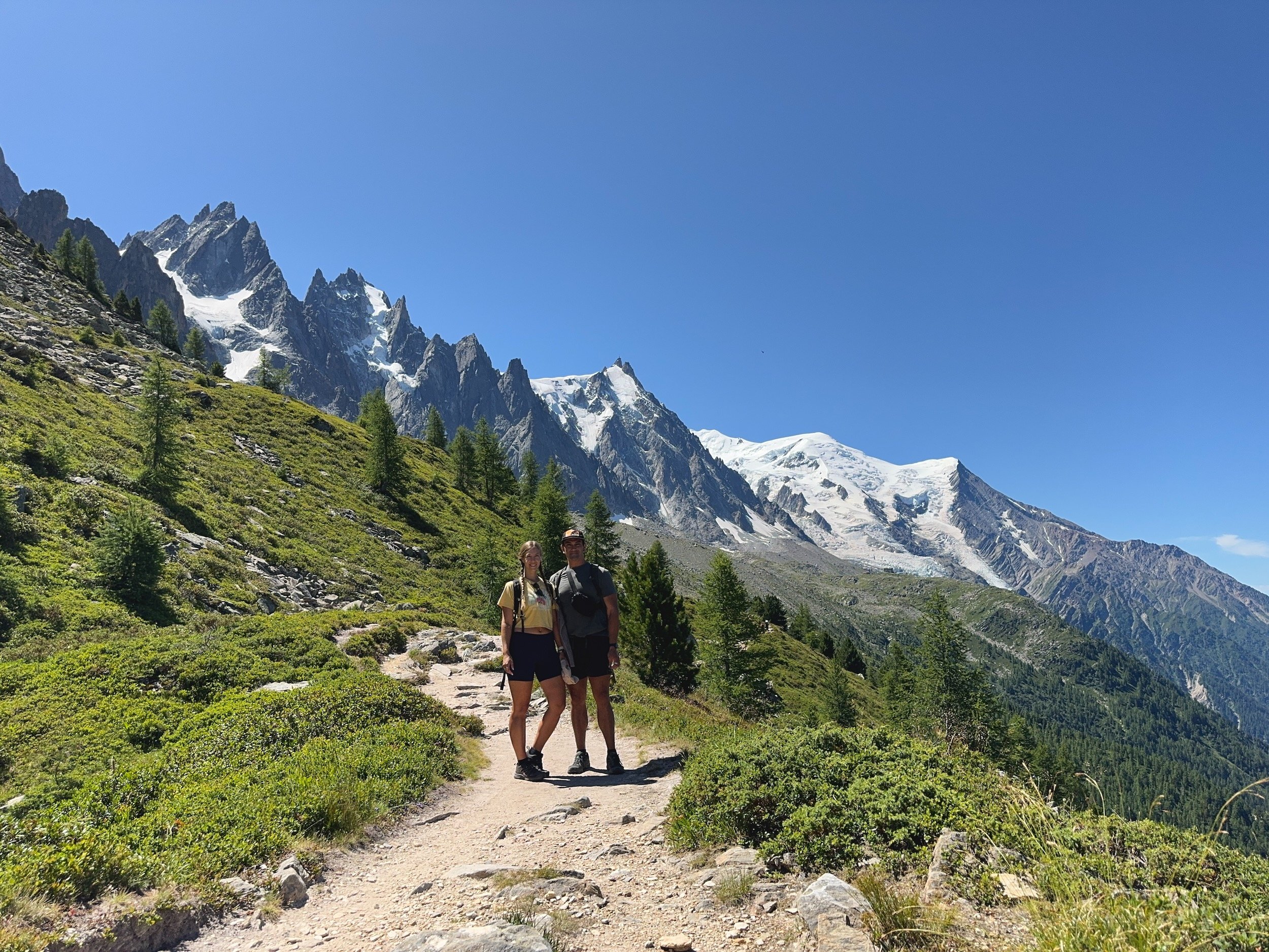 Nora and Trevor hiking on a mountain trail with the Mont Blanc massif in the background.