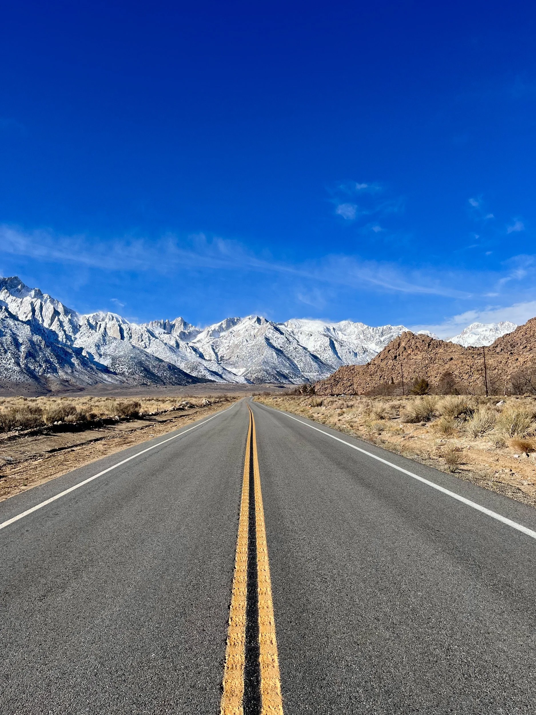 An empty road leading towards the snow-covered Sierra Nevada in Alabama Hills, California.