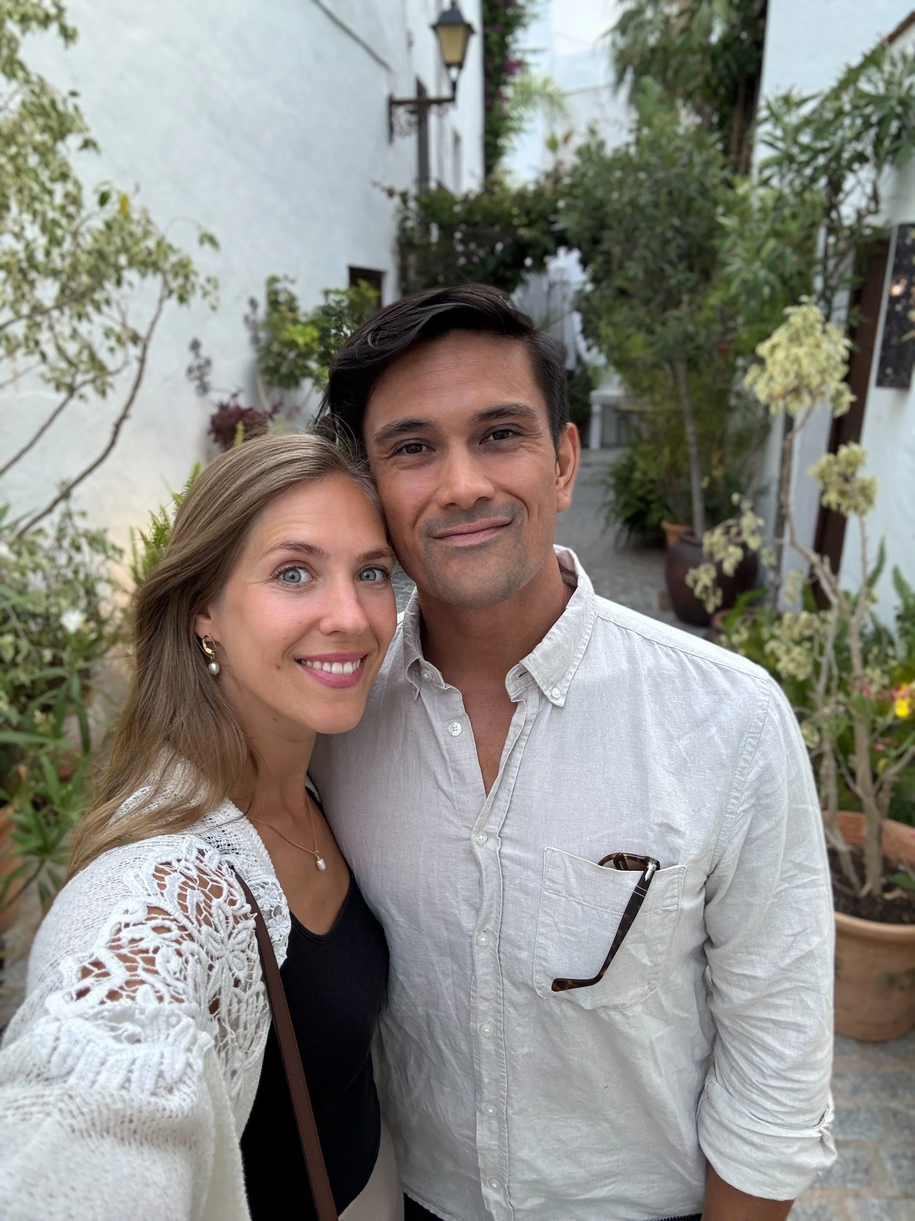 Nora and Trevor taking a selfie in a plant-filled courtyard while travelling in Vejer, Spain.