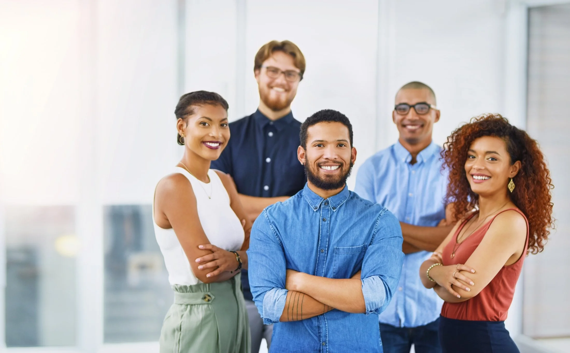 Group of five diverse professionals smiling in a modern office, with two women and three men.