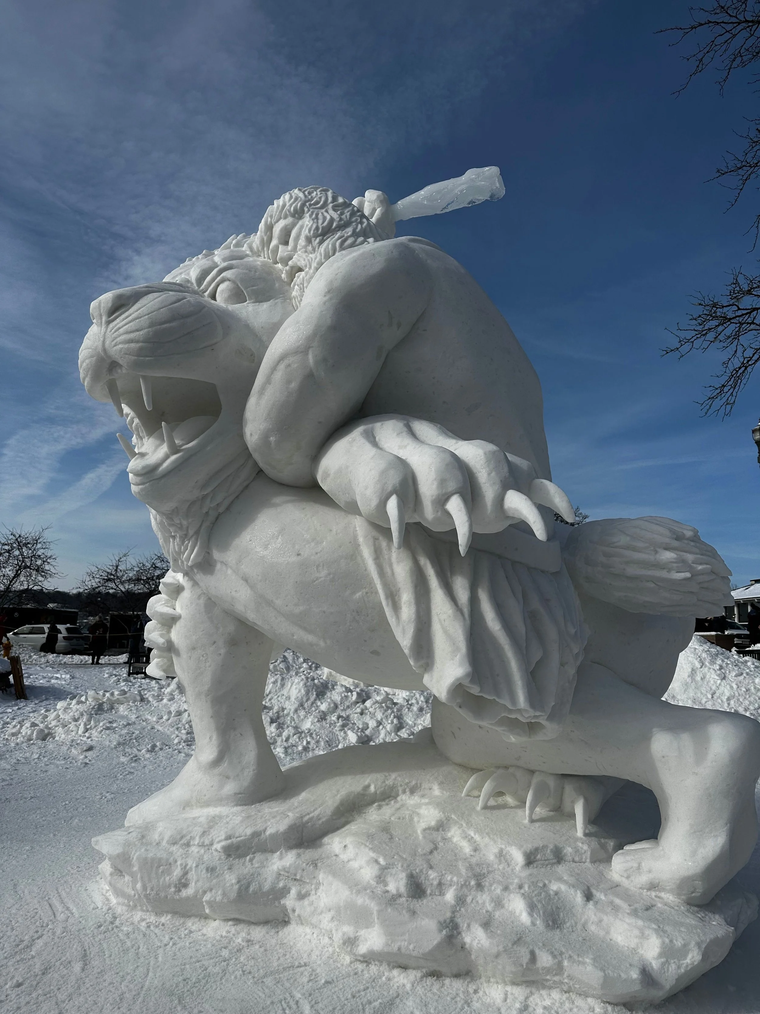 Snow sculpture of a fierce lion with a mane, standing on a snowy base during winter.