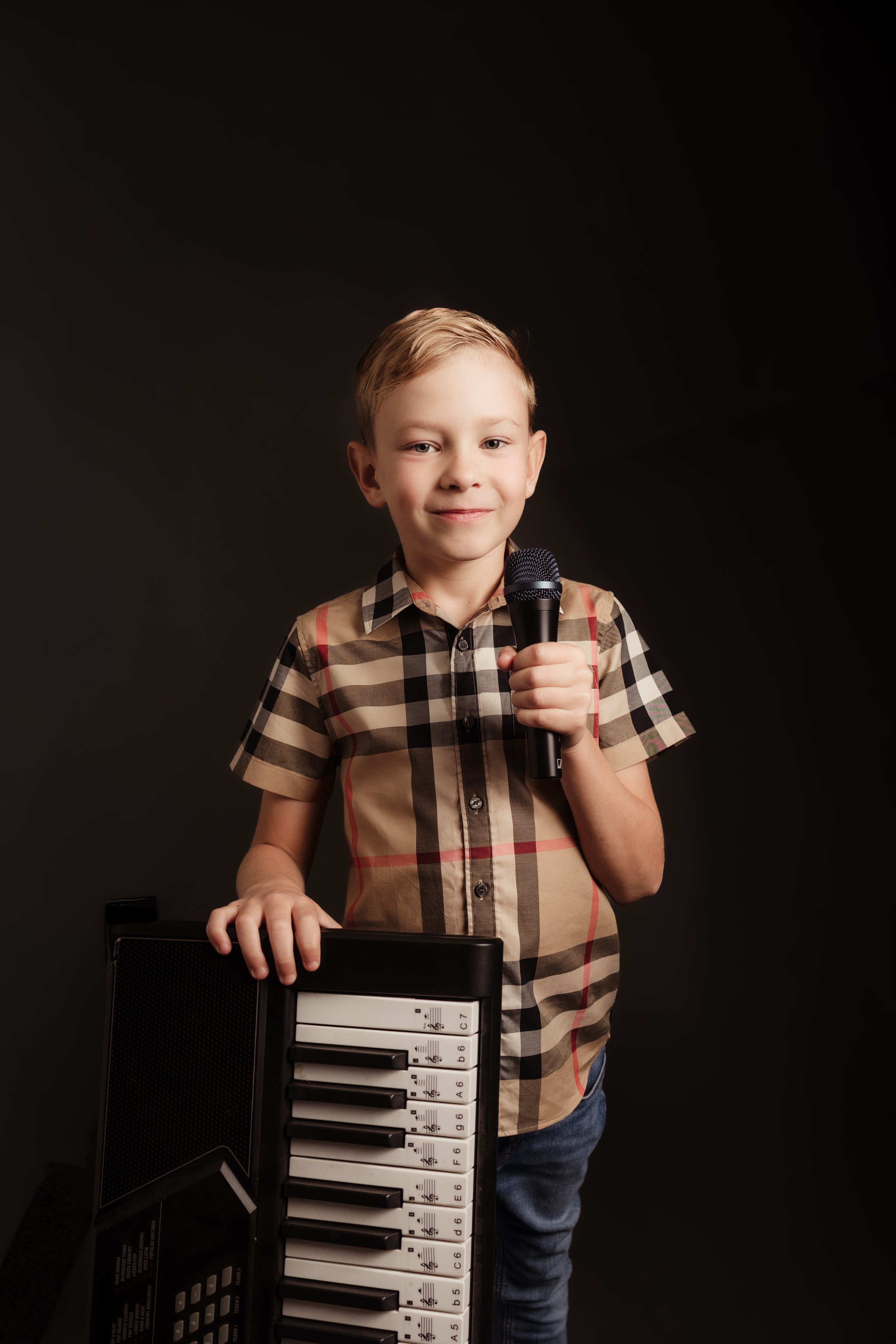 Young boy holding a microphone and standing next to a small electronic keyboard.