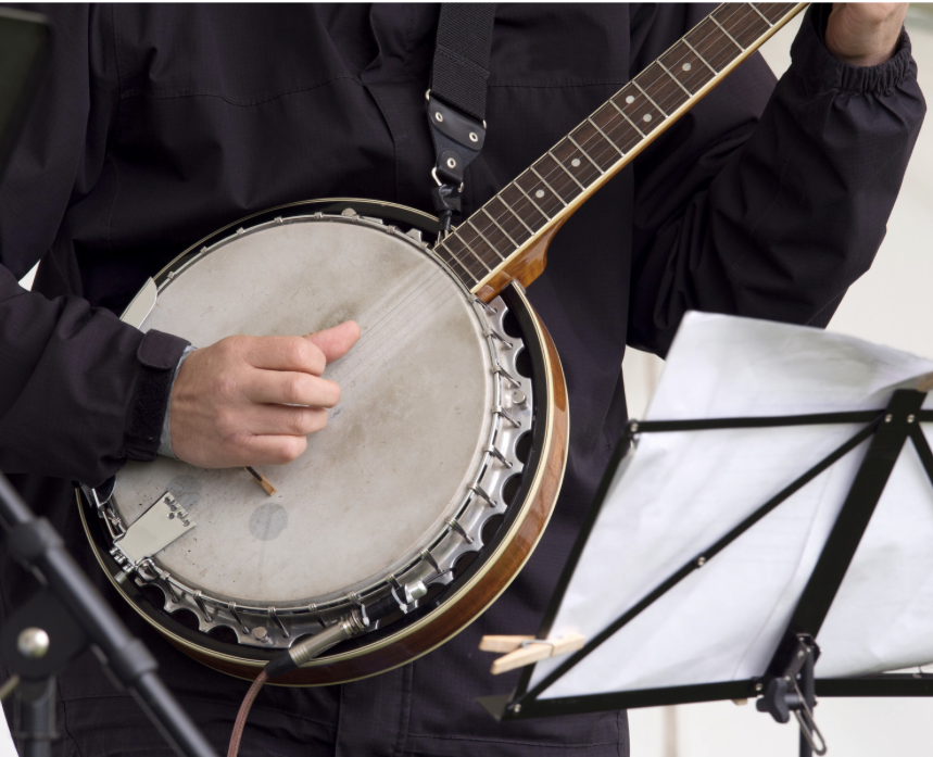Person playing banjo with sheet music on a stand nearby.