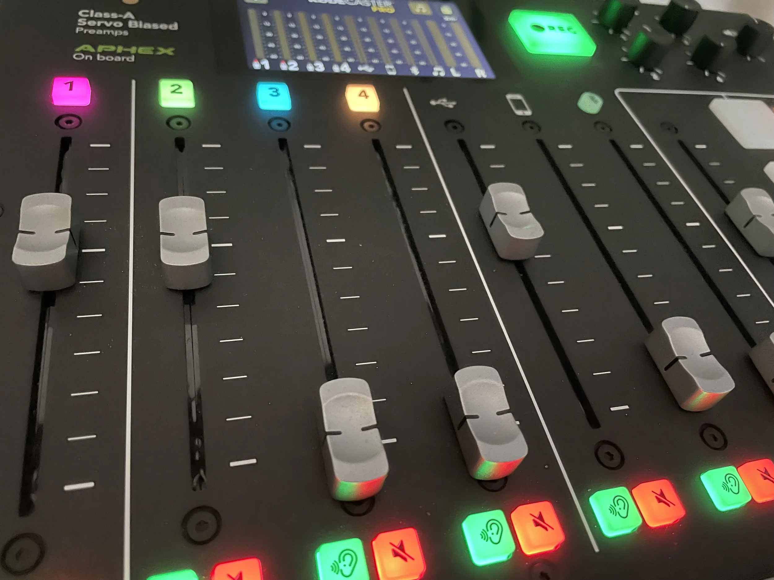 Nahaufnahme eines digitalen Mischpults mit mehreren Reglern, farbigen Knöpfen und Anzeigen.