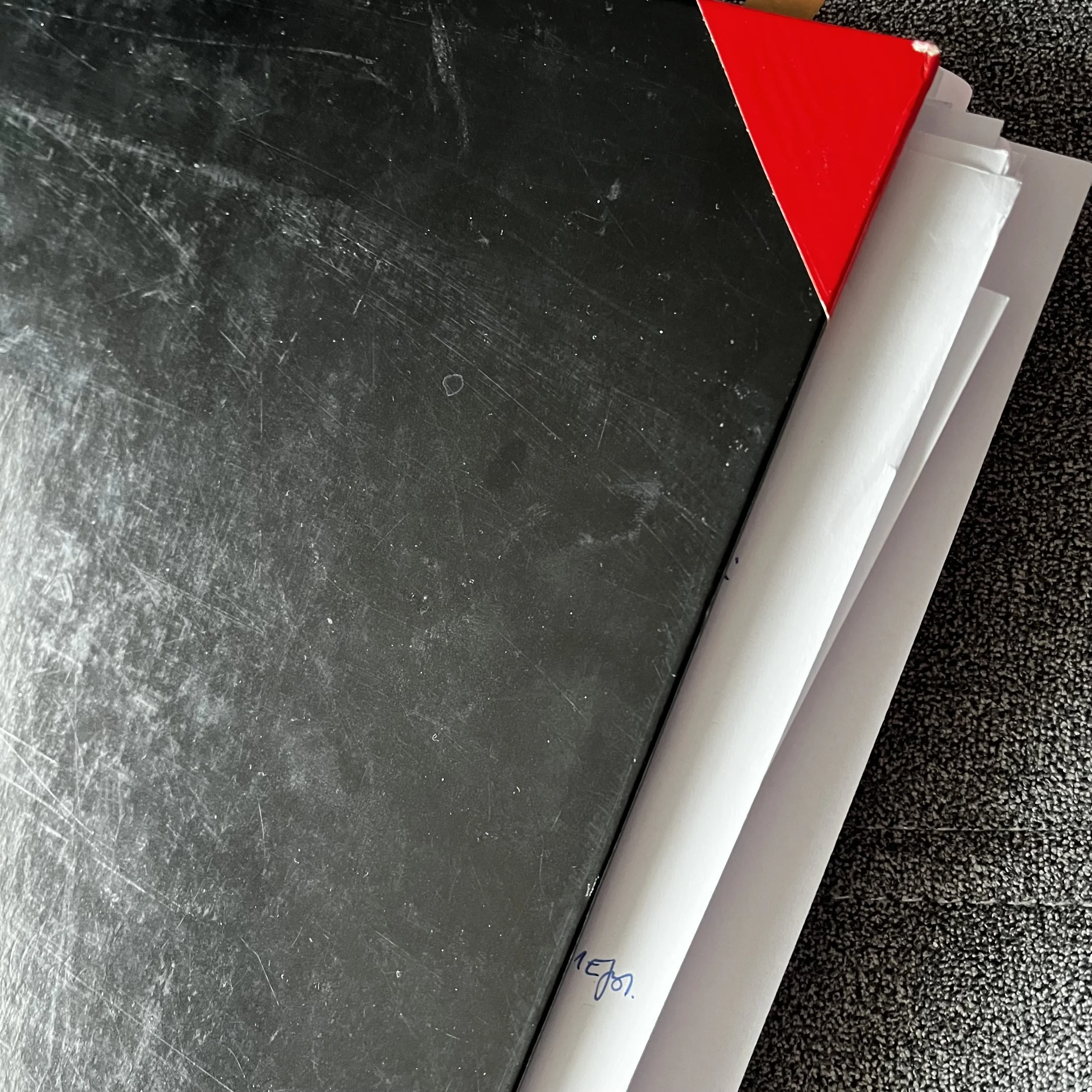 Schwarz glänzende Metallplatte mit Kratzern, neben weißen Notizblöcken, der oberste hat eine rote Ecke.