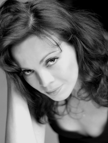 Black and white portrait of a woman with wavy hair, looking directly at the camera with a subtle smile.