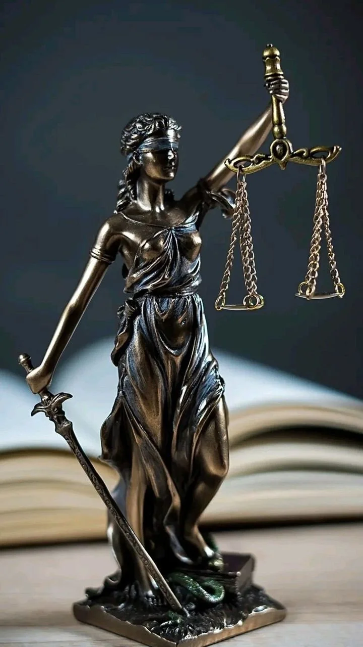 A metal statue of Lady Justice holding a sword in her right hand and a set of scales in her left, standing on a book with a snake coiled at her feet.