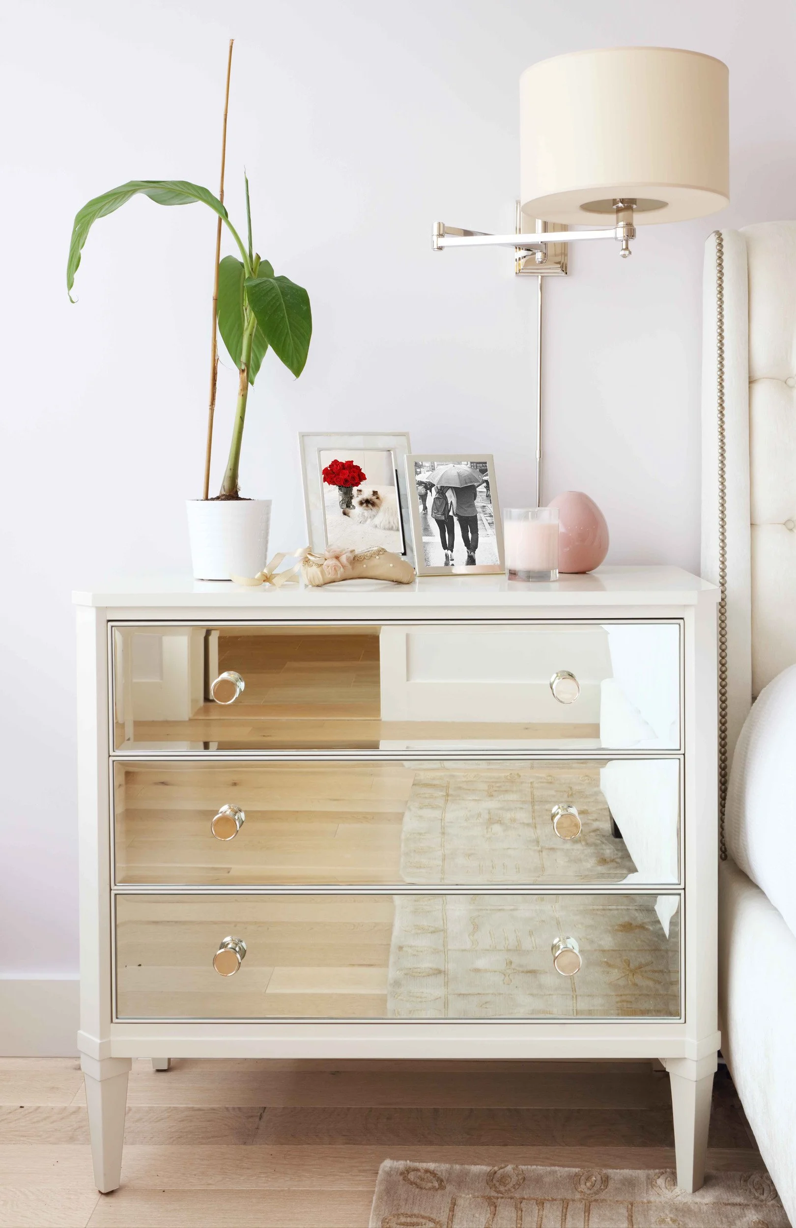 Mirrored nightstand detail with swing-arm wall sconce and personal accessories in Doyer Apartment in White Plains, NY.