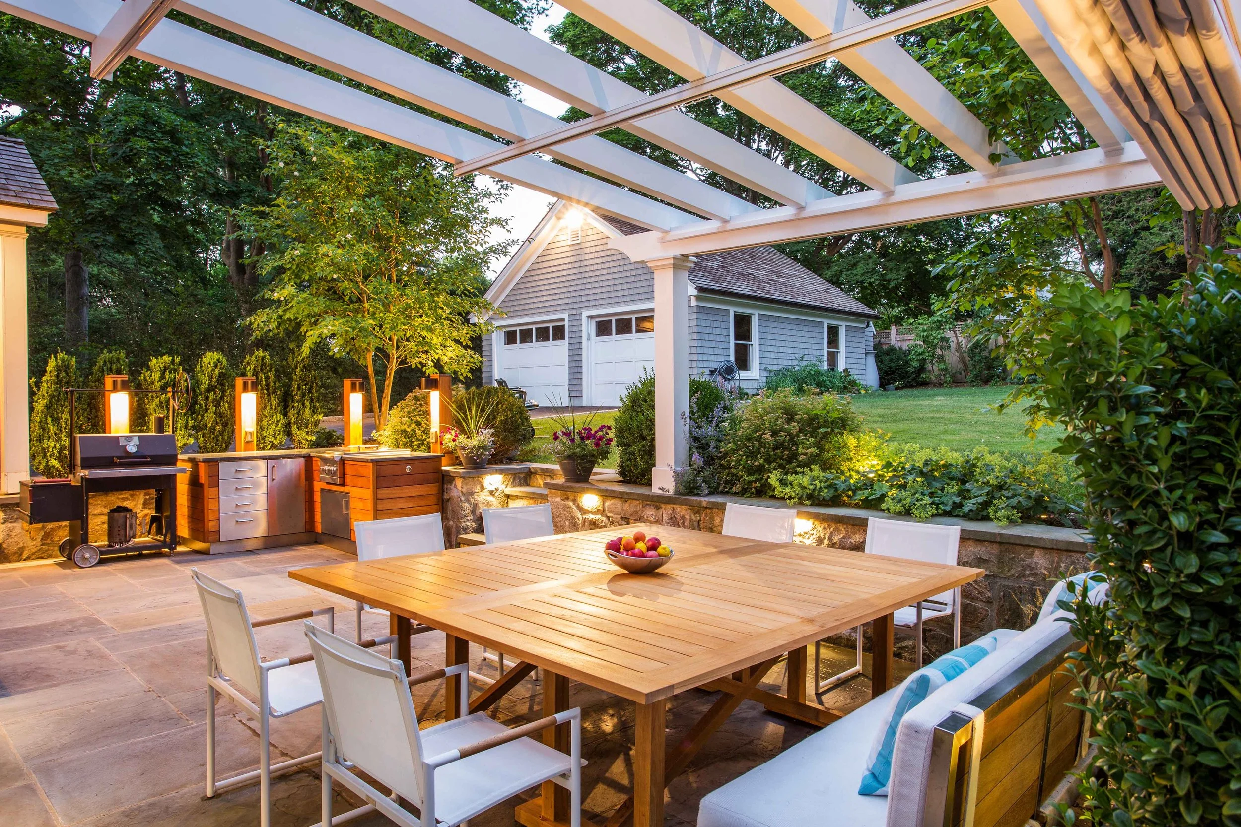 wide view of outdoor dining area with a vew towards outdoor kitchen at the Indian Field Outdoor project in Greenwich, CT, designed by Luminosus Designs.