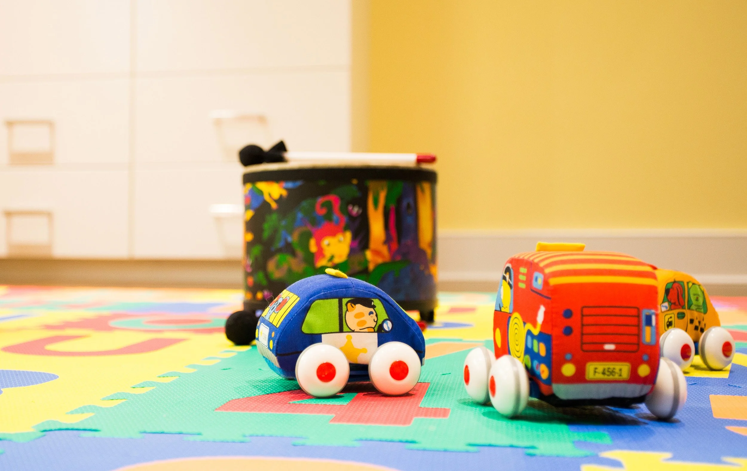 Detail shot of toy cars arranged on a colorful foam play mat in the basement play area.