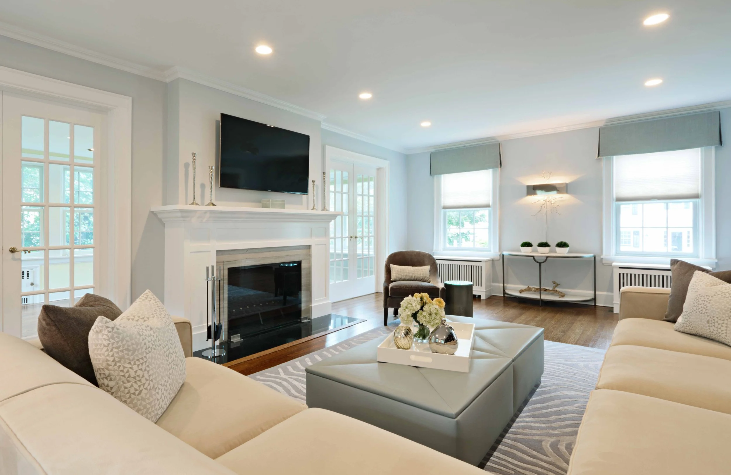 Wide view of a refined family room with custom fireplace mantel, neutral sectional seating, layered textiles, and tailored window treatments.