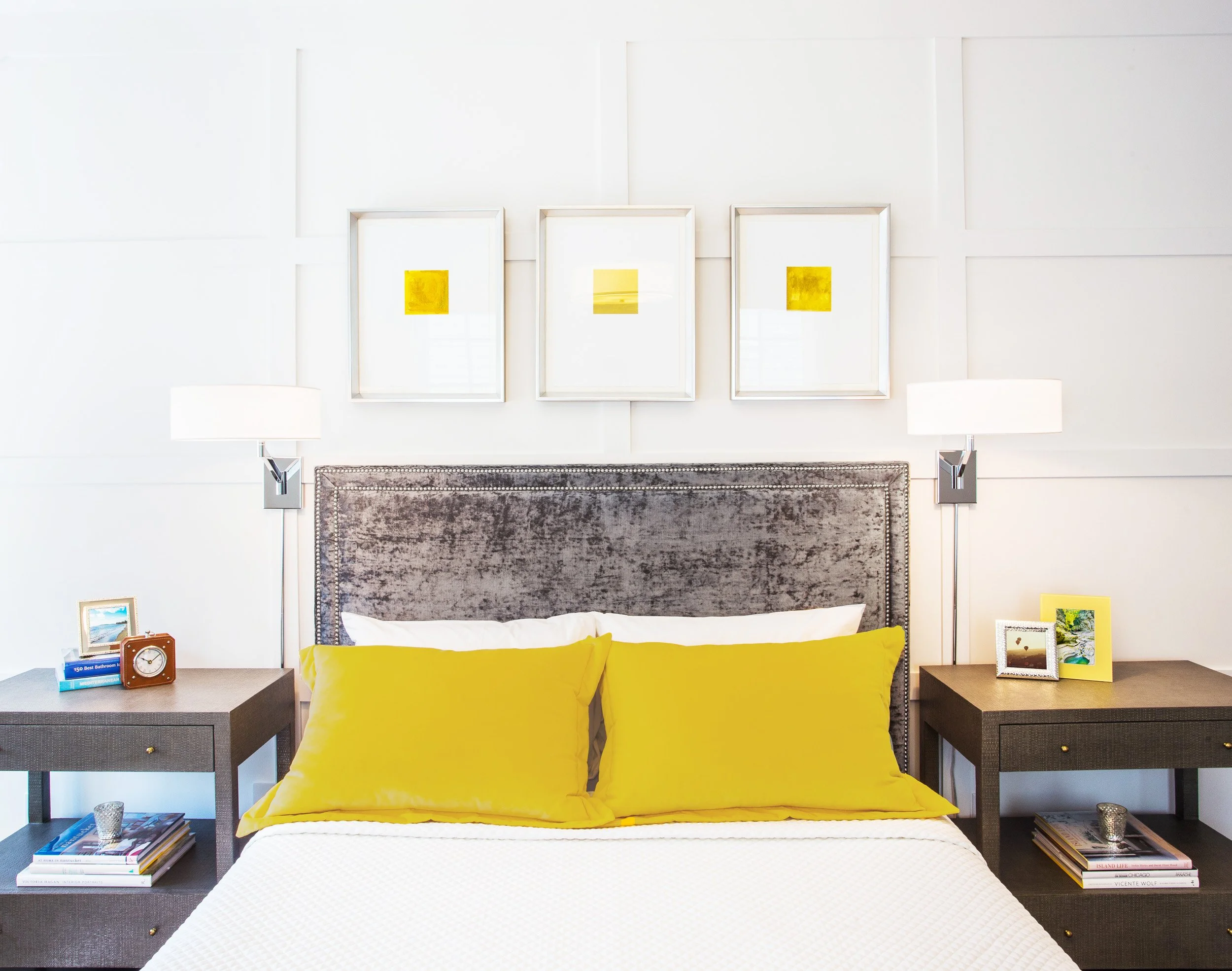 Close-up of the guest bed with an upholstered headboard, wall sconces, and yellow accent pillows against panel molding.