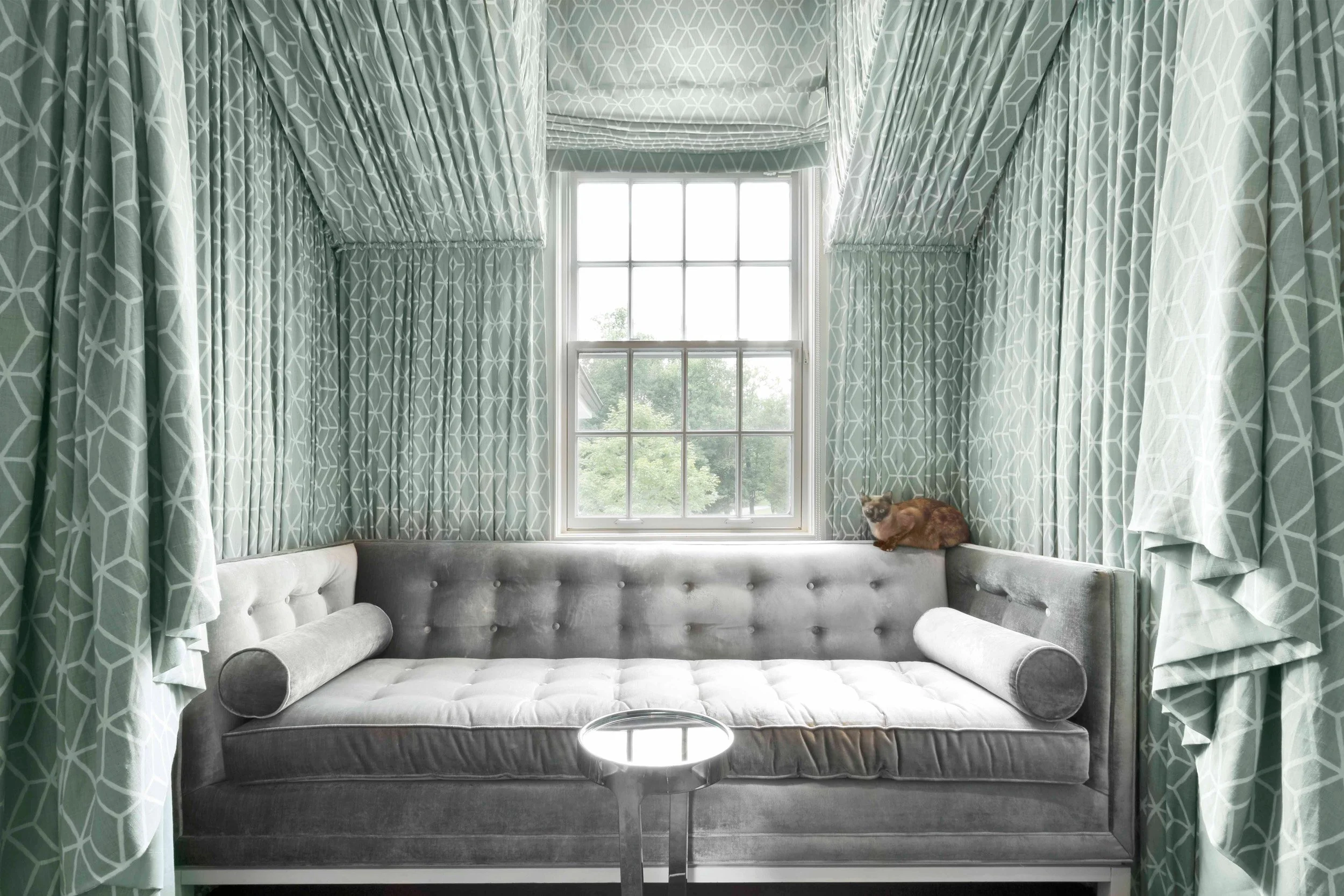 Reading nook at the Meeting House in Greenwich, CT featuring a custom upholstered window seat framed by patterned drapery.