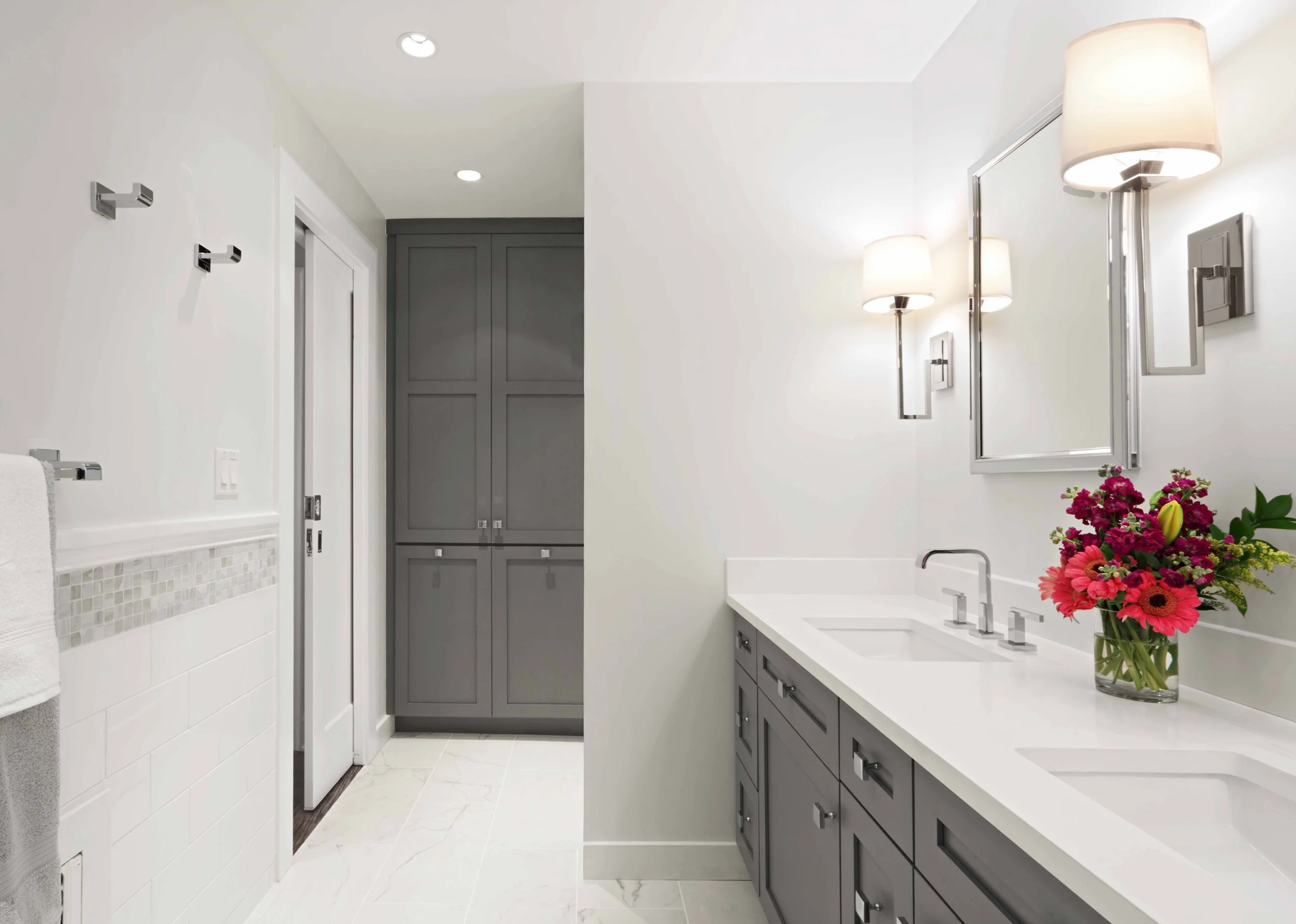 Wide view of a primary bathroom with custom double vanity, marble flooring, and custom linen cabinet  in Scarsdale, NY.