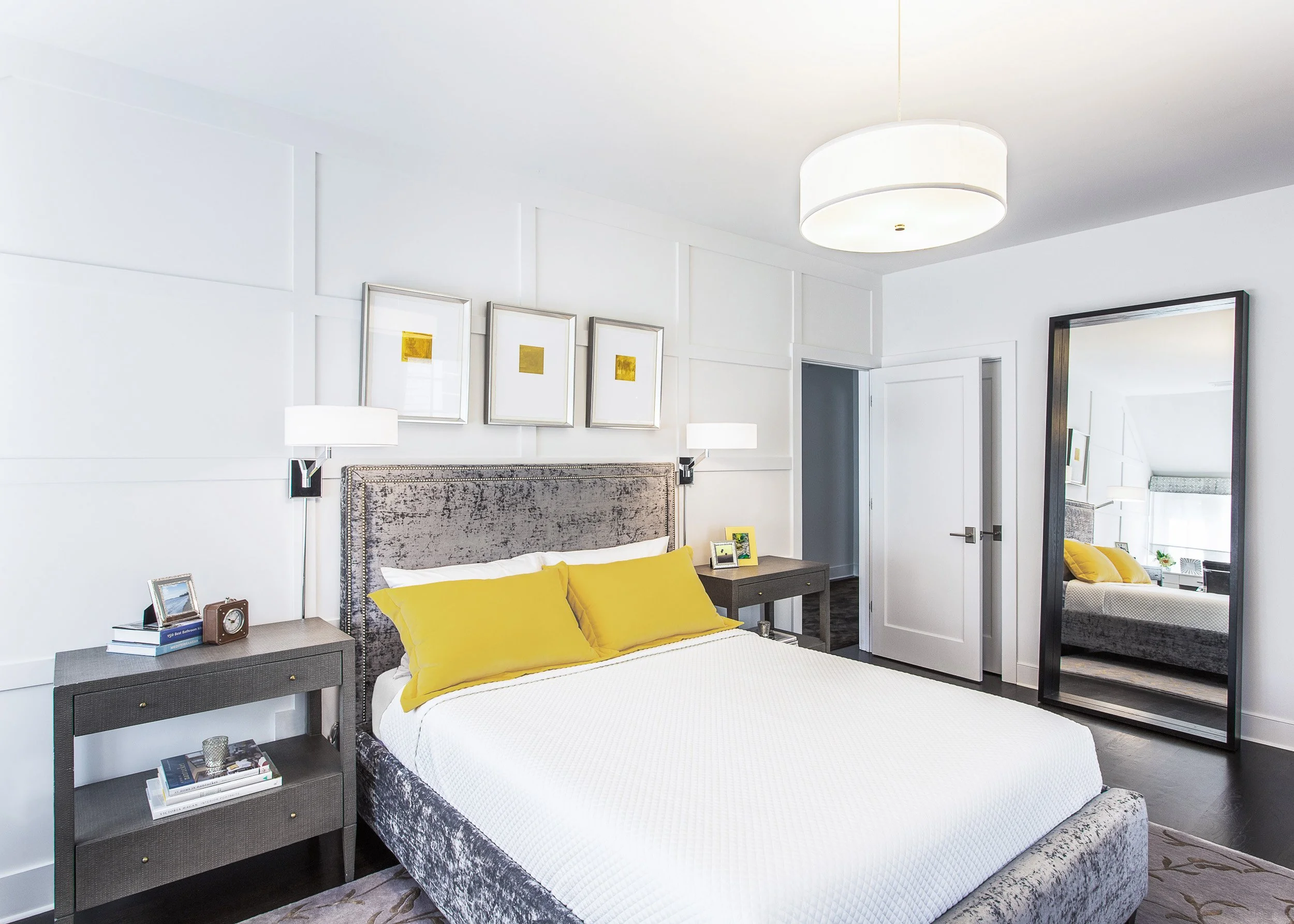 Wide view of a guest bedroom featuring an upholstered bed, paneled accent wall, wall sconces, and soft neutral bedding in Kensett House in Darien, CT. Designed by Luminosus Designs.