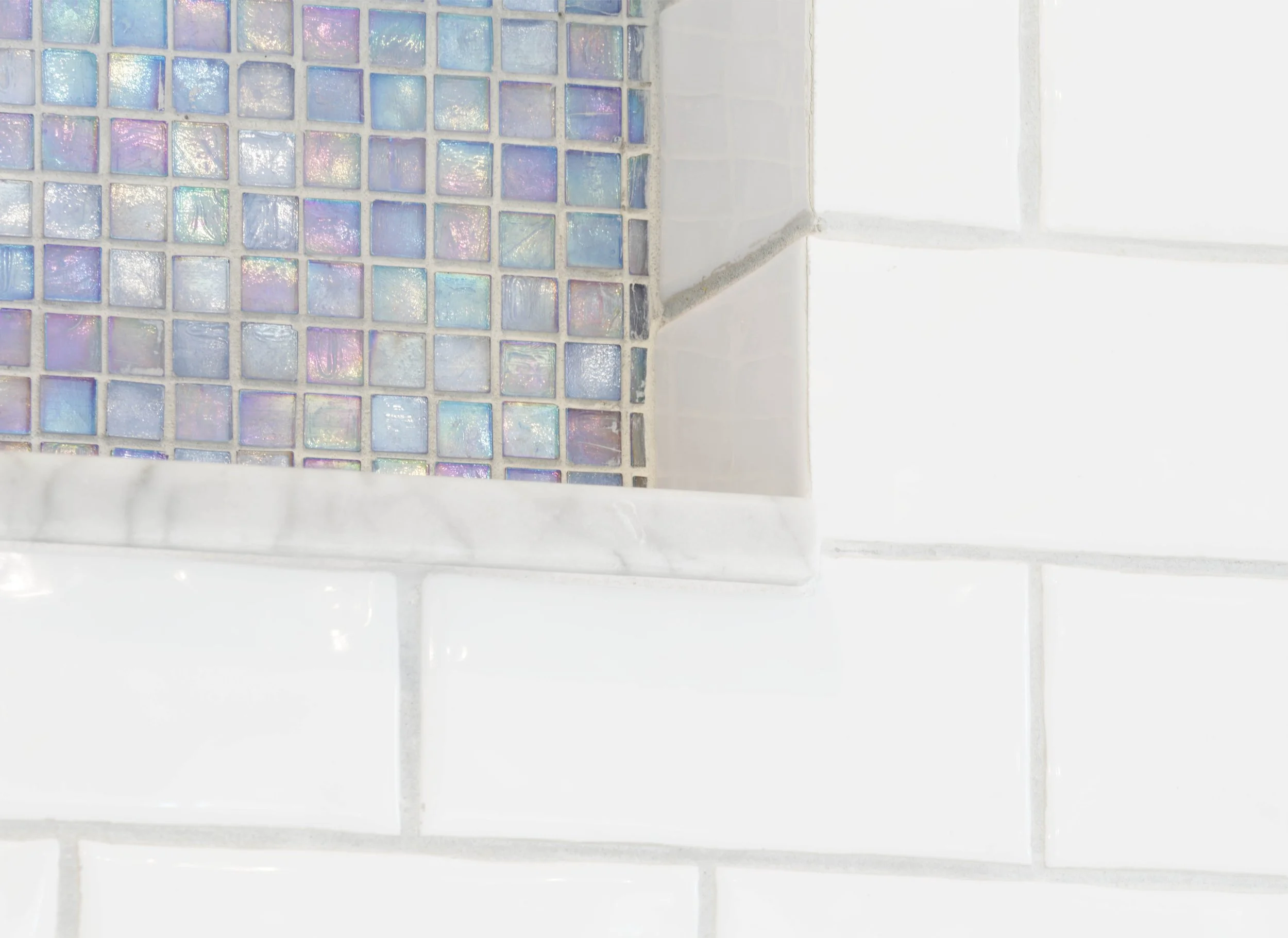 Close-up of tiled shower niche with iridescent mosaic.