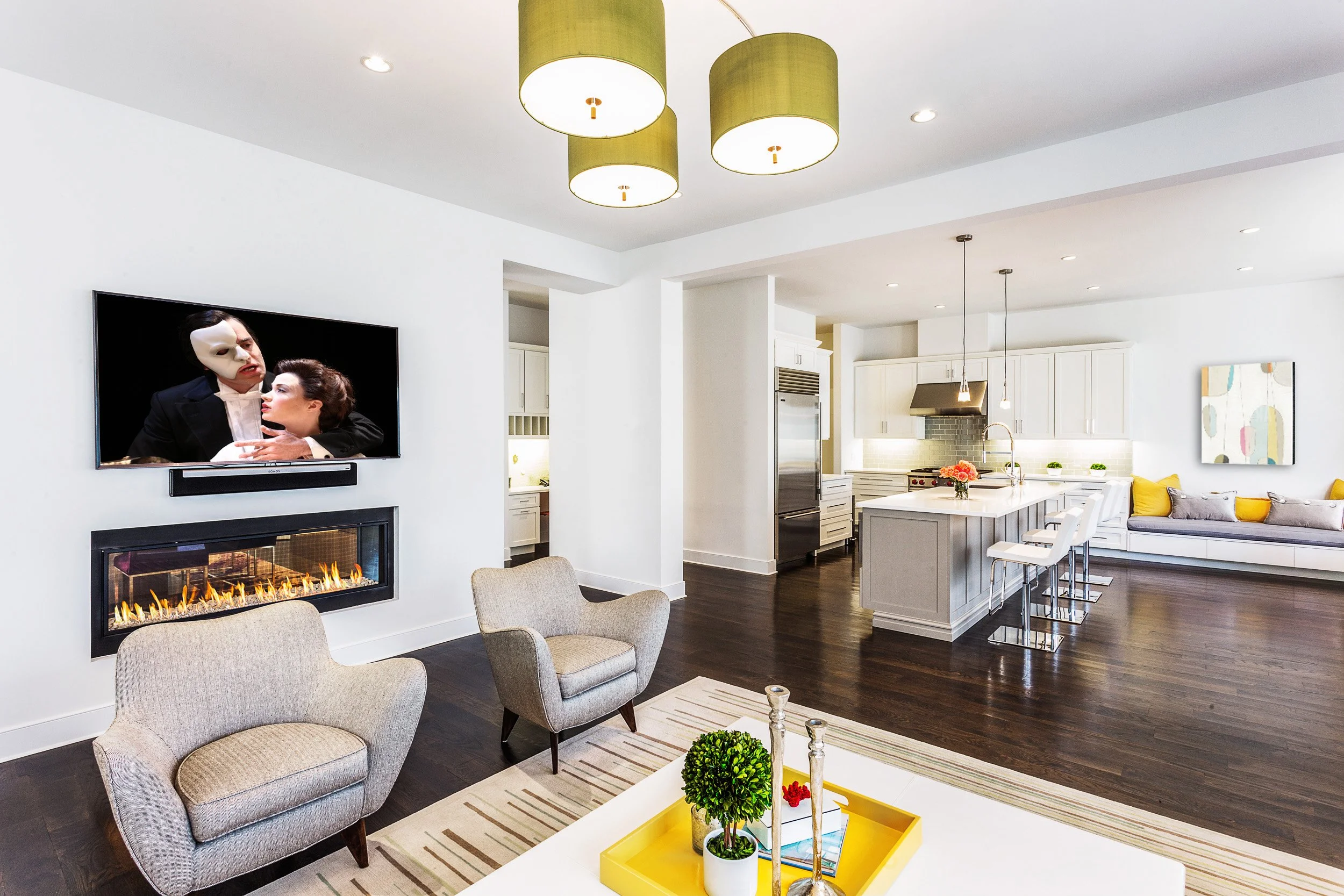 Wide view of the family room showing a linear fireplace wall, comfortable seating, and the kitchen beyond for easy entertaining flow in Kensett House in Darien, CT. 