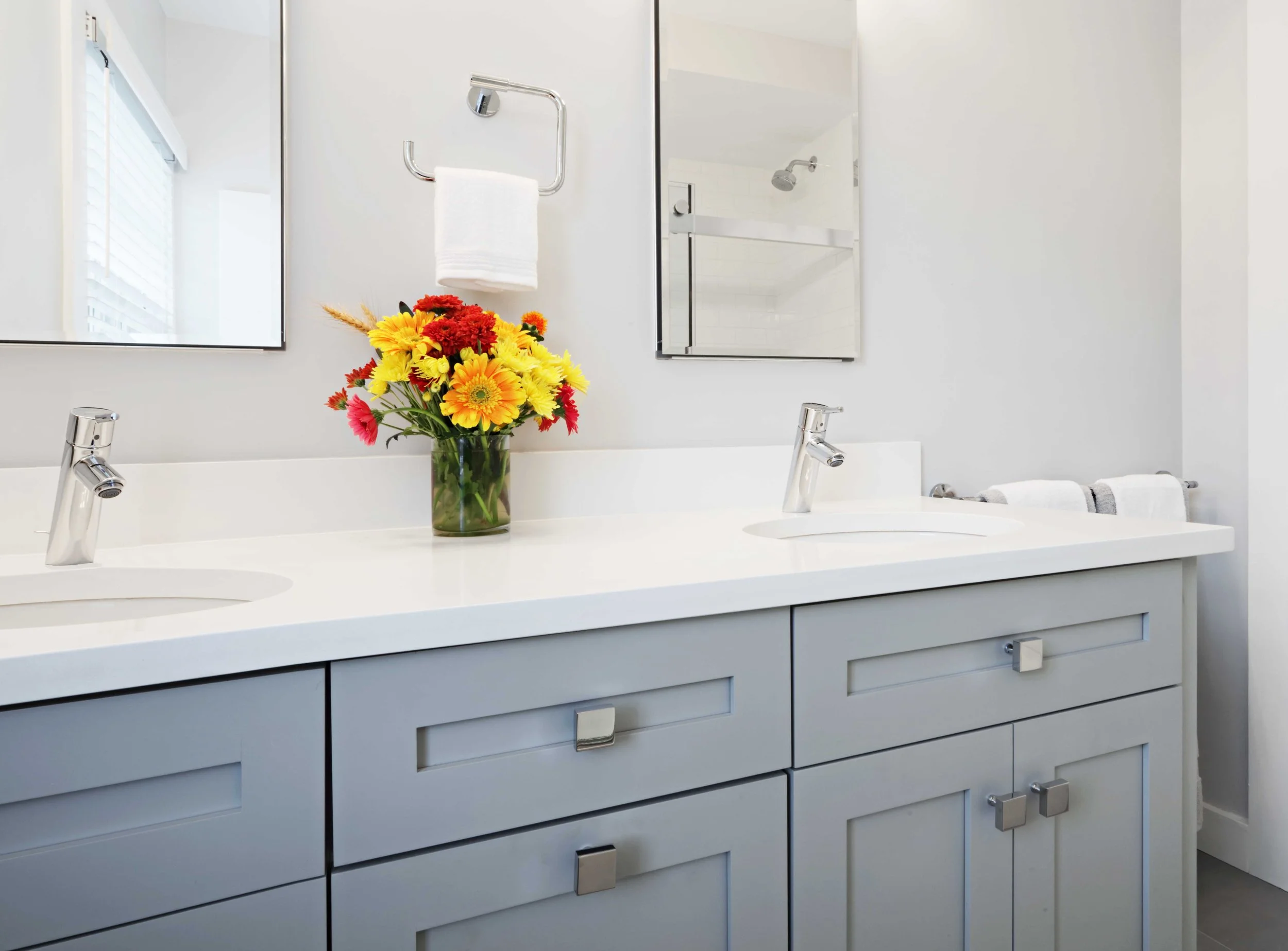 Close-up of a custom gray bathroom vanity with integrated storage, white quartz countertop, and modern chrome faucet  in Scarsdale, NY.