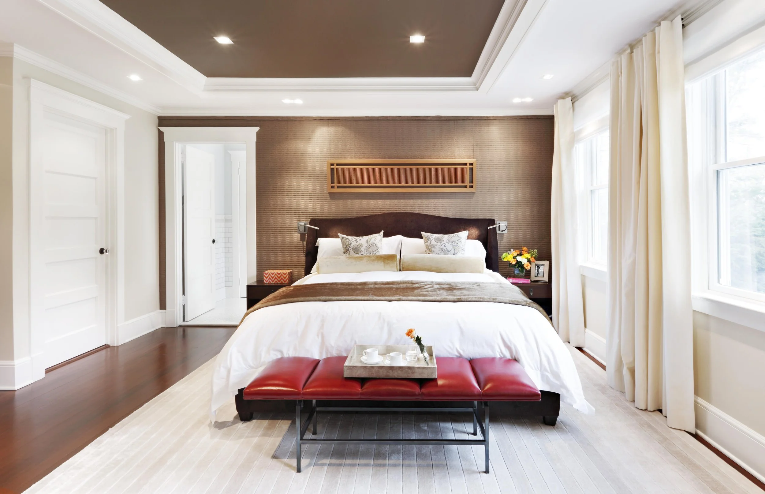 Wide view of primary bedroom with custom window treatments and metal frame bench.