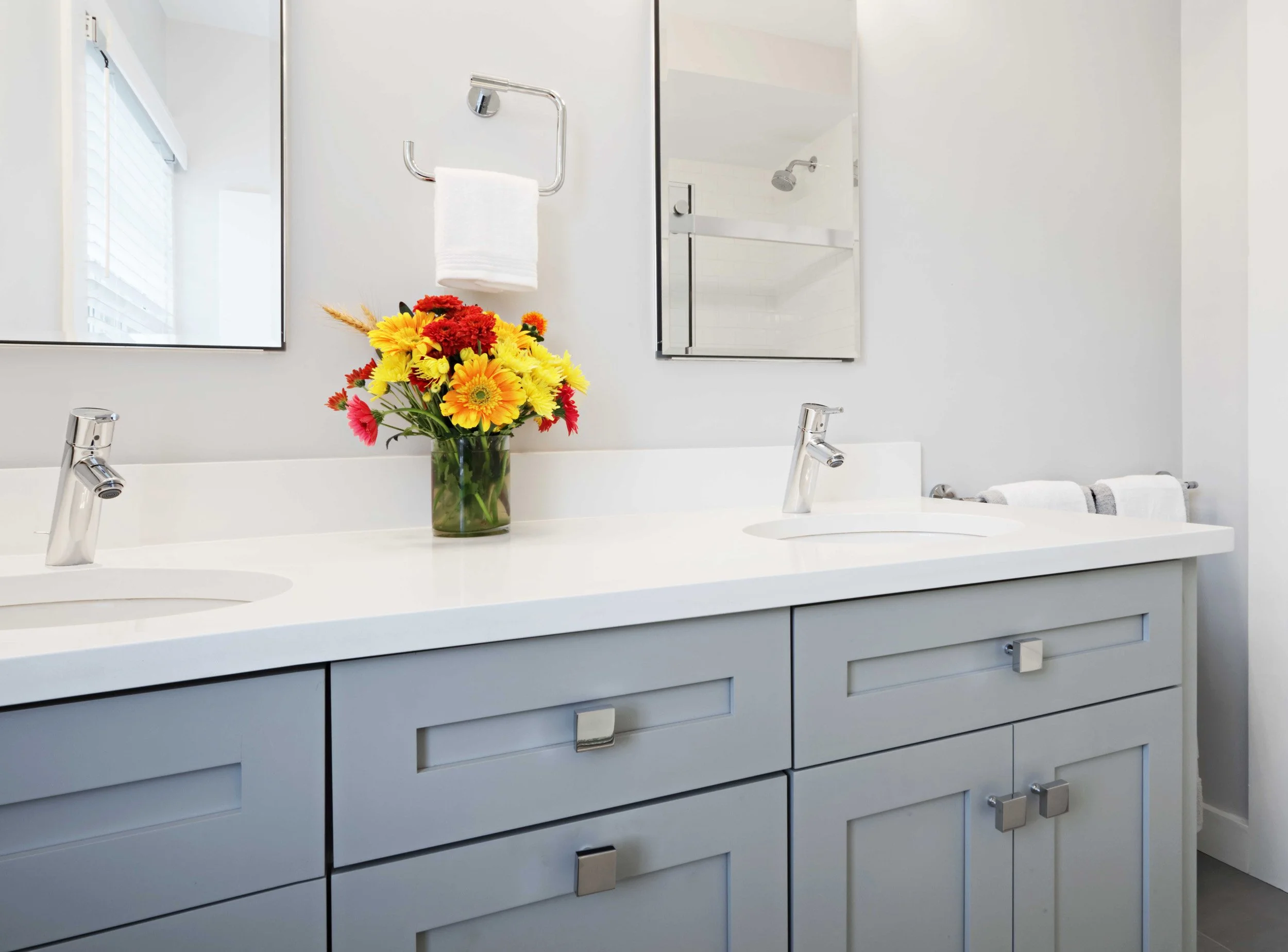 Close-up of a custom gray bathroom vanity with integrated storage, white quartz countertop, and modern chrome faucet  in Scarsdale, NY.