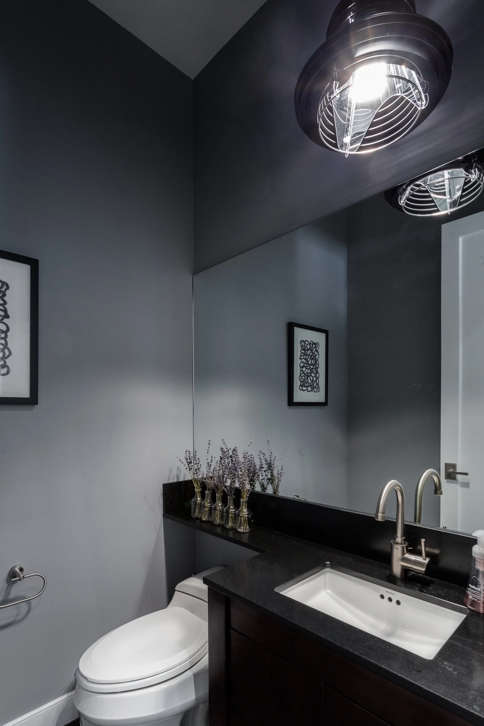 Wide view of a powder room with a floating dark vanity, black countertop, modern faucet, and industrial cage ceiling lights in Kensett House in Darien, CT.  Designed by Luminosus Designs.