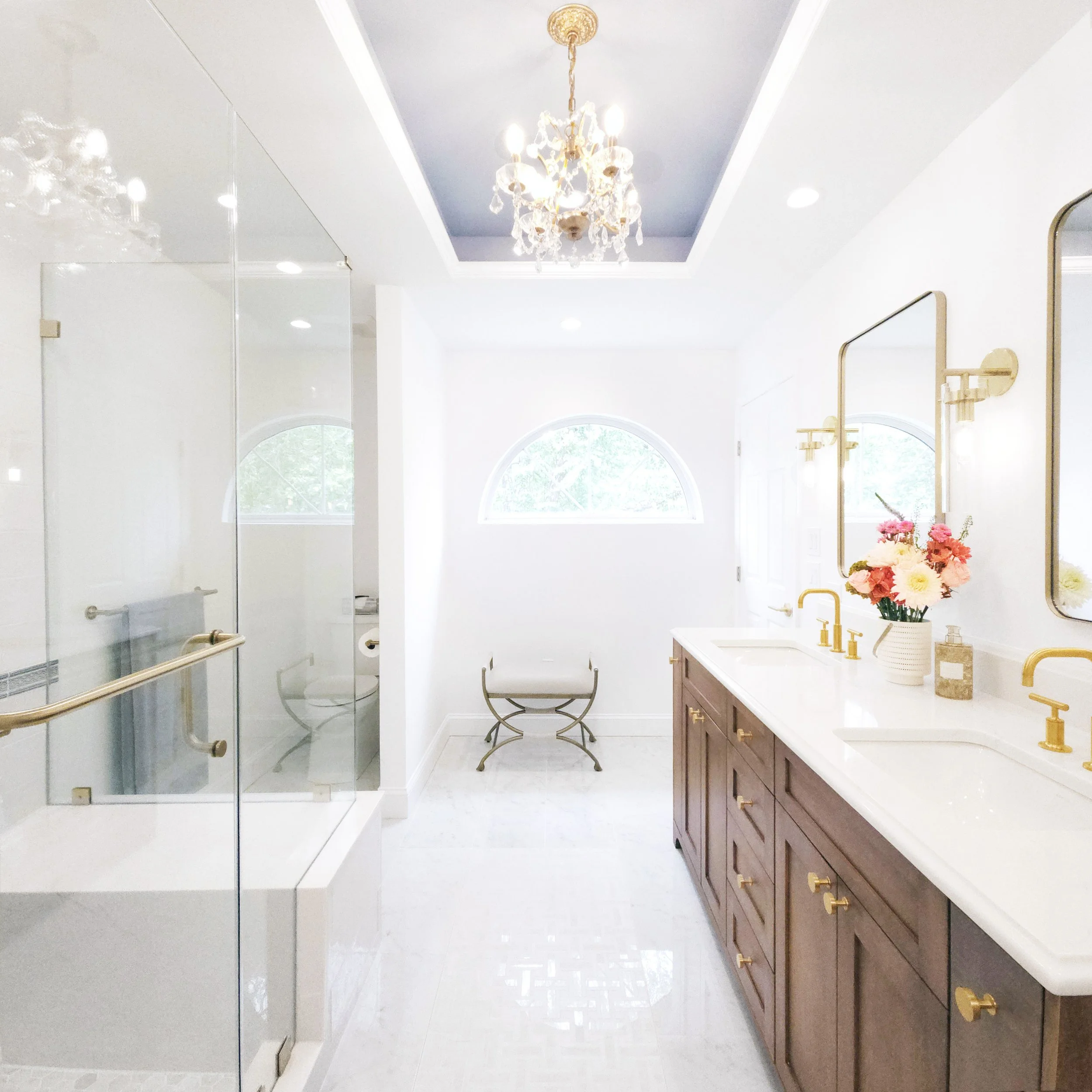Full primary bathroom overview in Carlyle Court in Princeton, NJ featuring double vanity, glass shower, brass fixtures, and arched window by Luminosus Designs.
