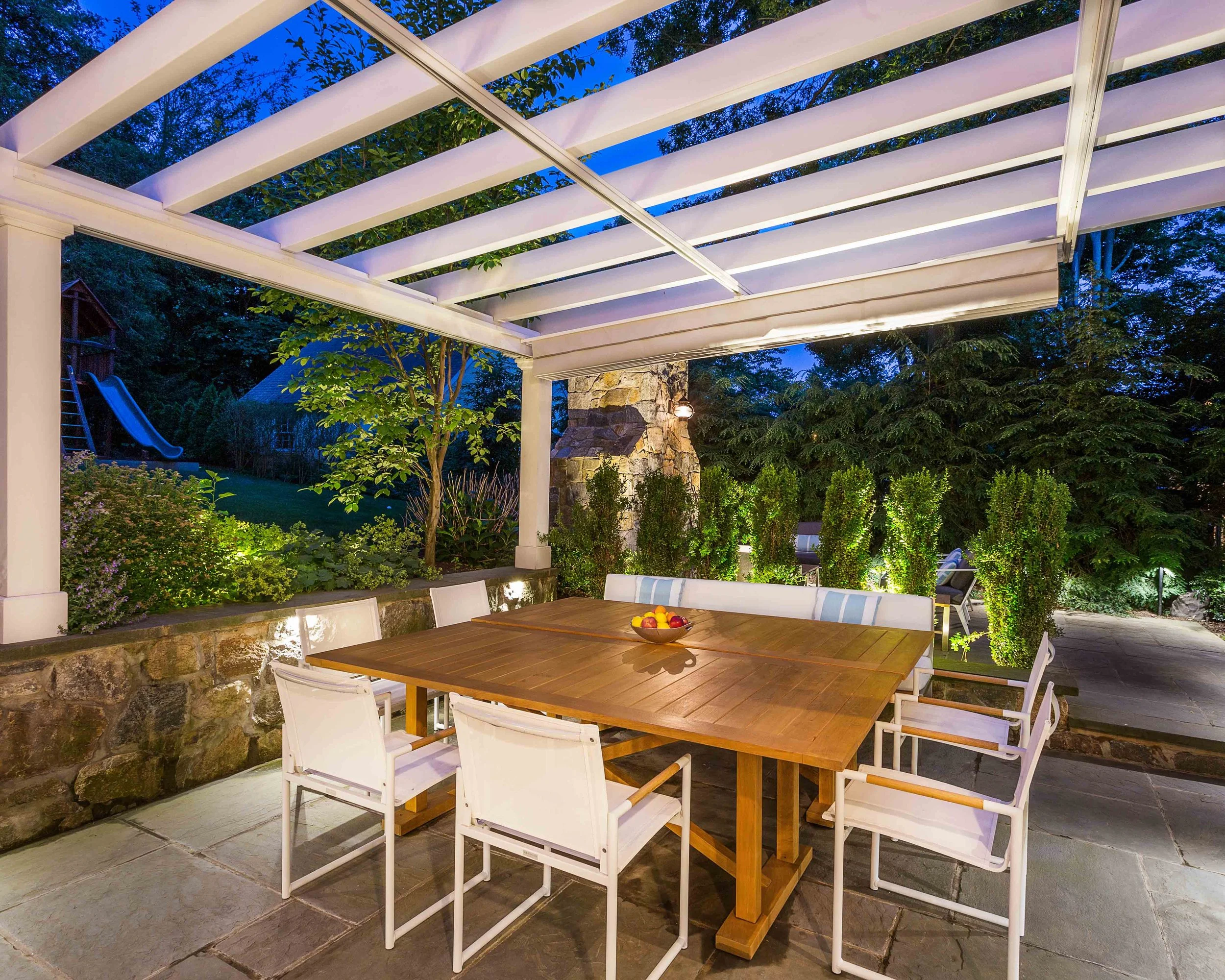 Evening view of outdoor dining area with pergola shade retracted at the Indian Field Outdoor project in Greenwich, CT.