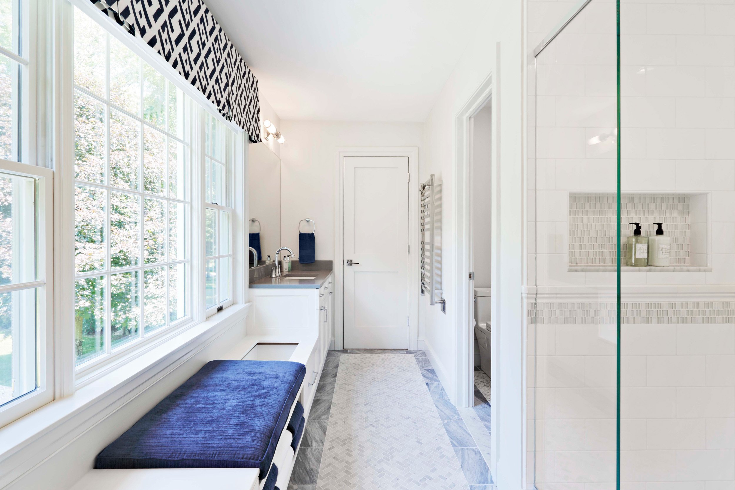 Wide view of a bright Jack and Jack bathroom at the Dann Farm home in Pound Ridge, NY designed by Luminosus Designs, featuring white cabinetry, marble tile flooring, and built-in bench seating.