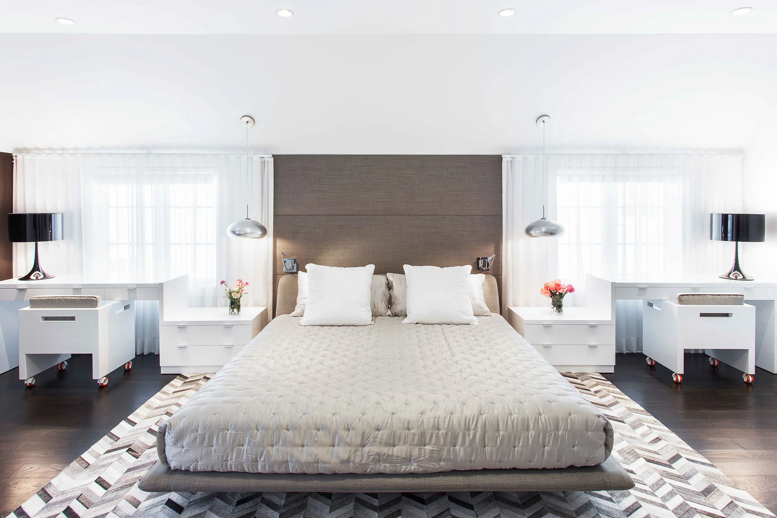 Wide view of the primary bedroom bed wall with symmetrical nightstands, pendant lights, and layered bedding.