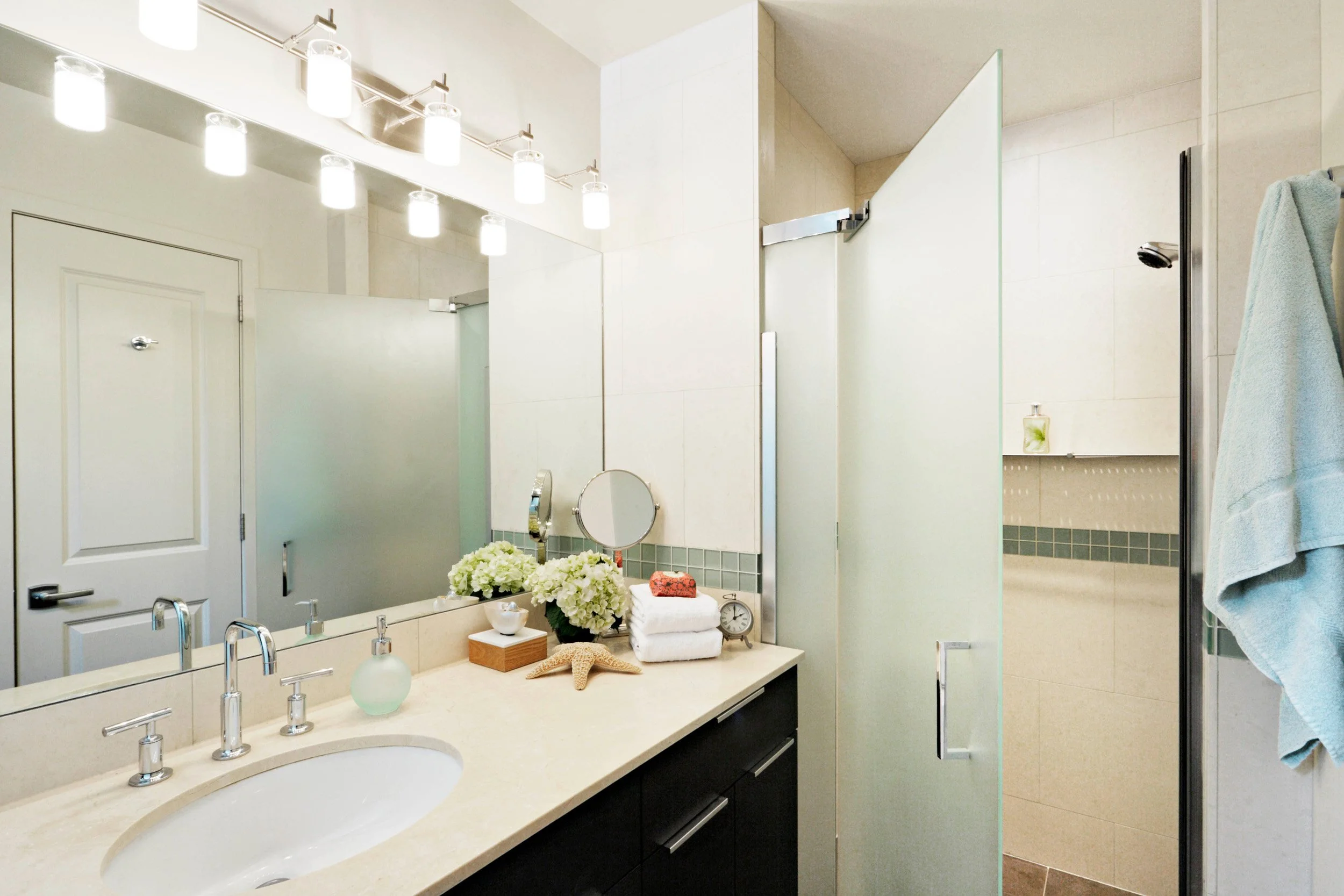 Close-up of bathroom at the Muliner House in Bronx, NY featuring a dark wood vanity and cream color stone countertop designed by Luminosus Designs.